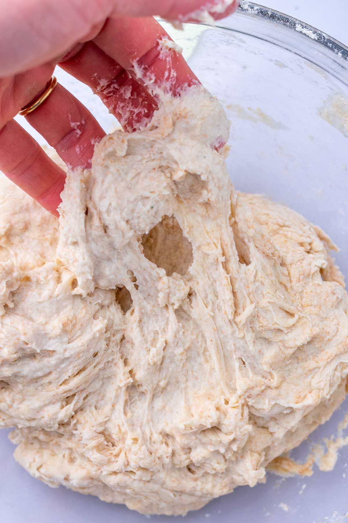 Hand pulling a very wet and shaggy dough in bowl after no autolyse.