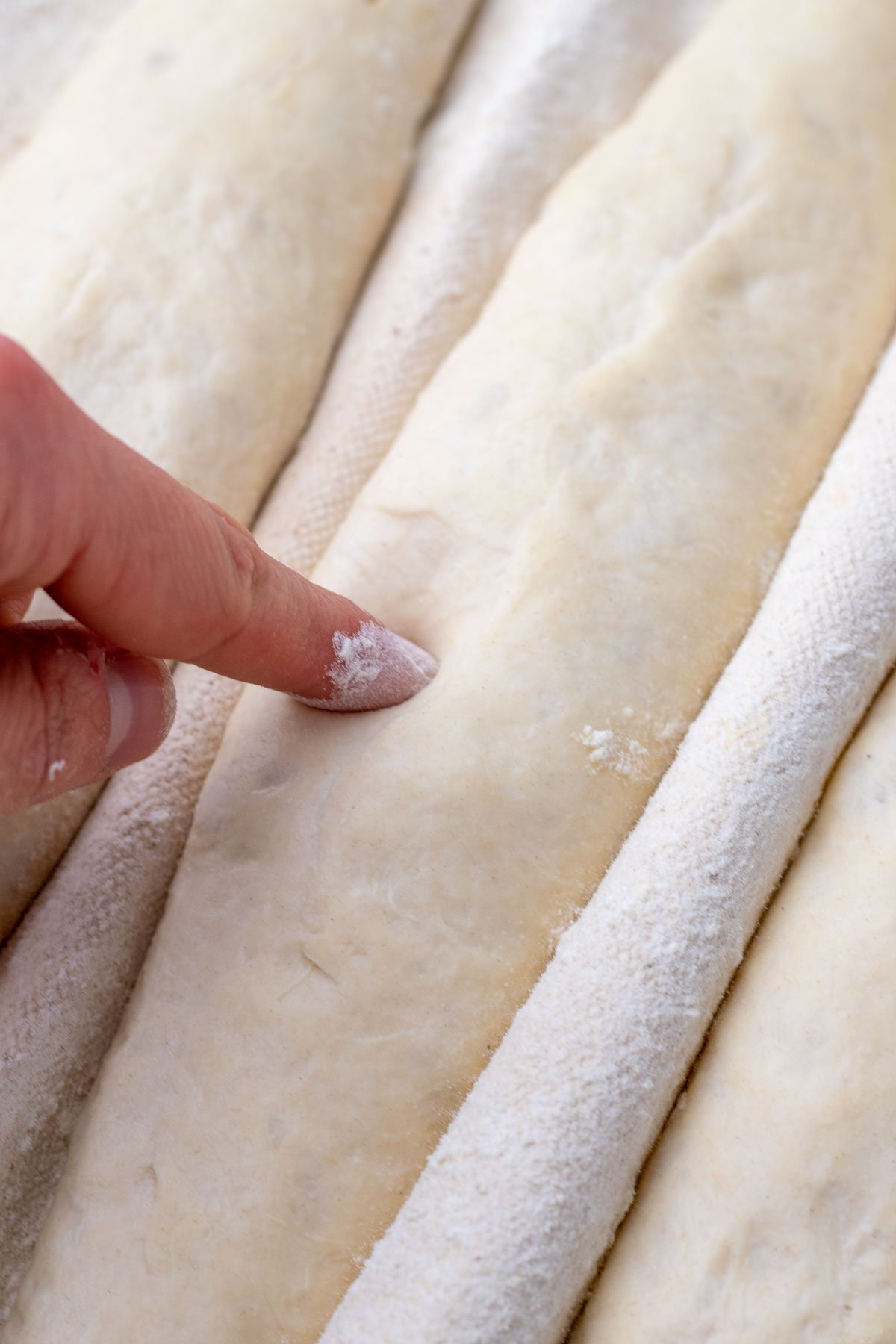 Finger poke test of a proofed sourdough baguette in couche.