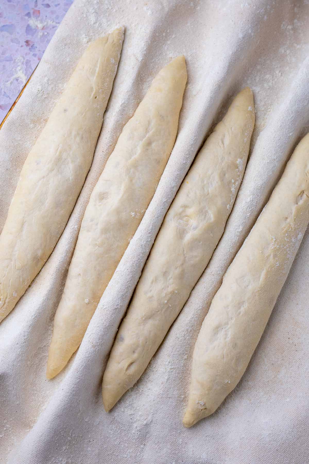 Four proofed sourdough baguettes in a baker's couche.