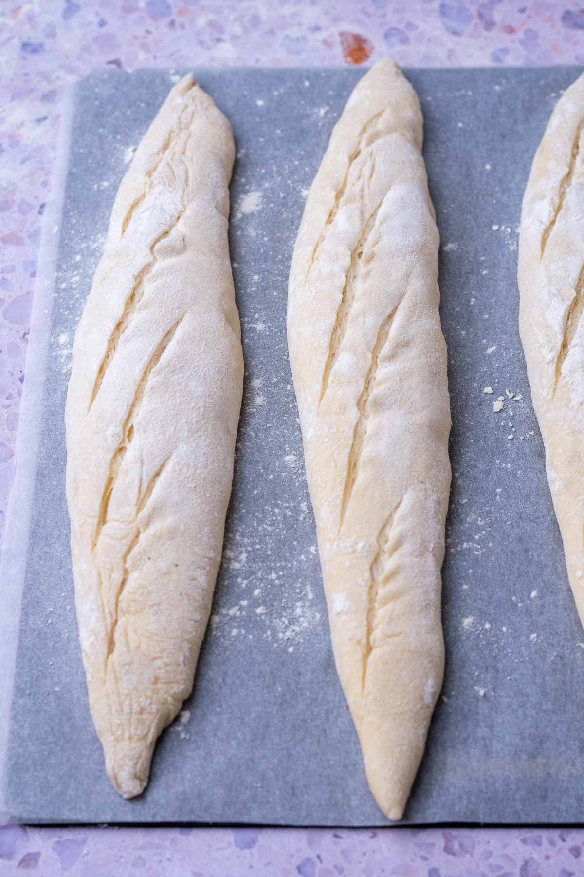 Scored sourdough baguettes on a baking steel and parchment paper.