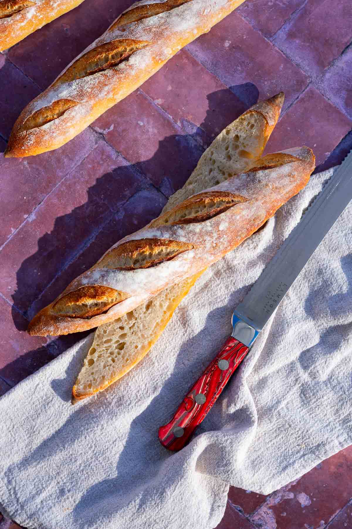 Sliced sourdough baguette with crumb and a bread knife.