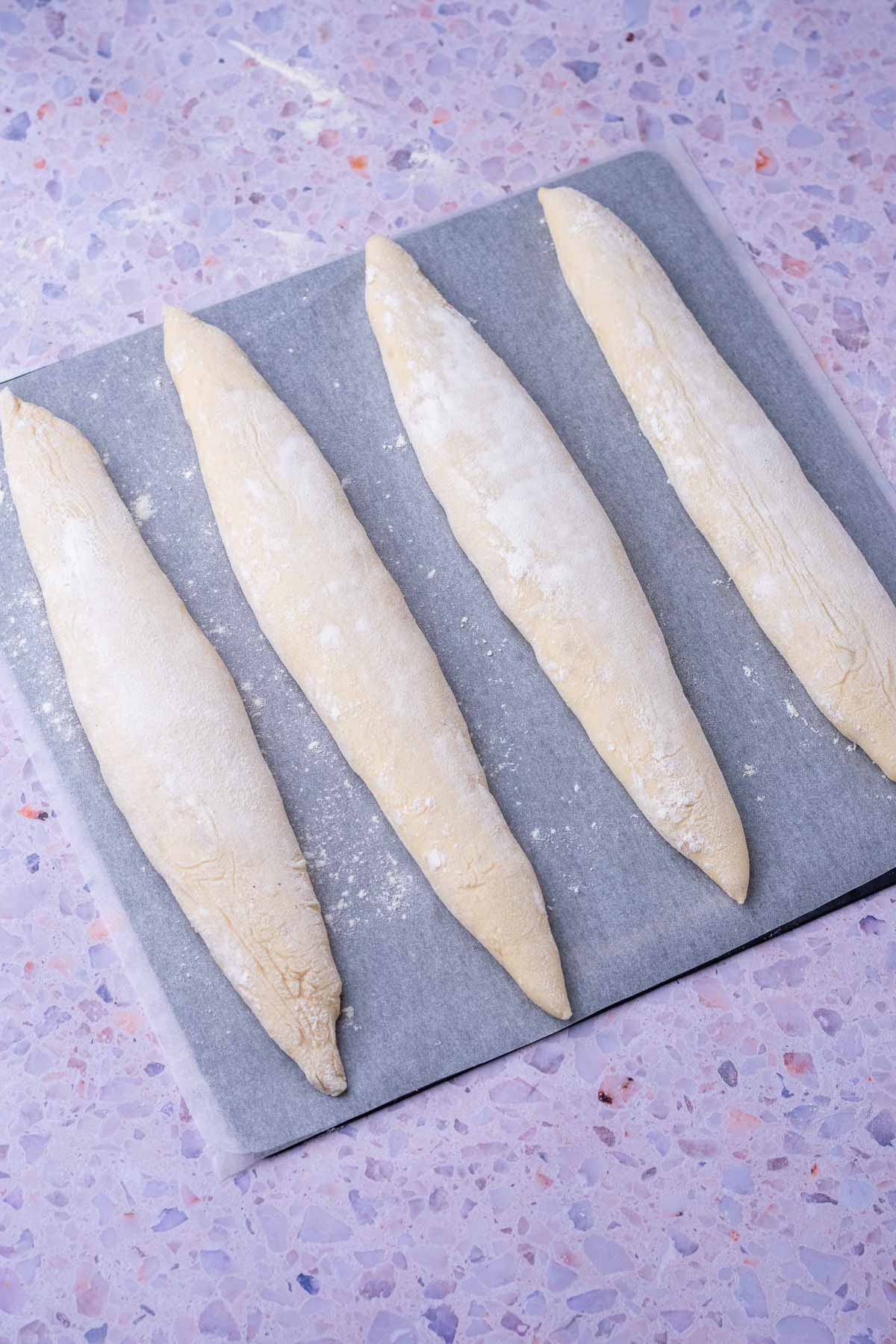 Four unbaked sourdough baguettes on a baking steel.
