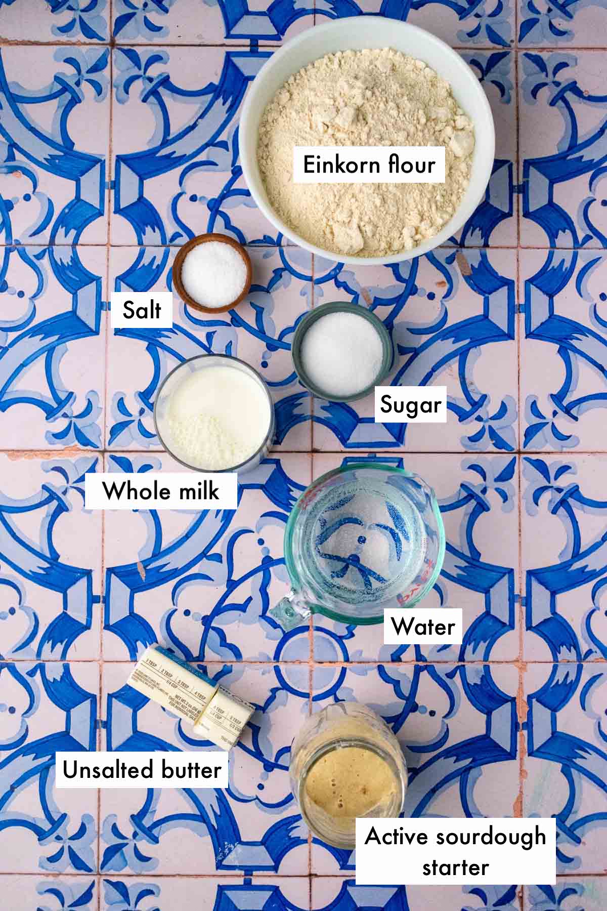 Labeled bowls of ingredients needed for einkorn sourdough sandwich bread including einkorn flour, salt, sugar, water, whole milk, butter, and active sourdough starter.