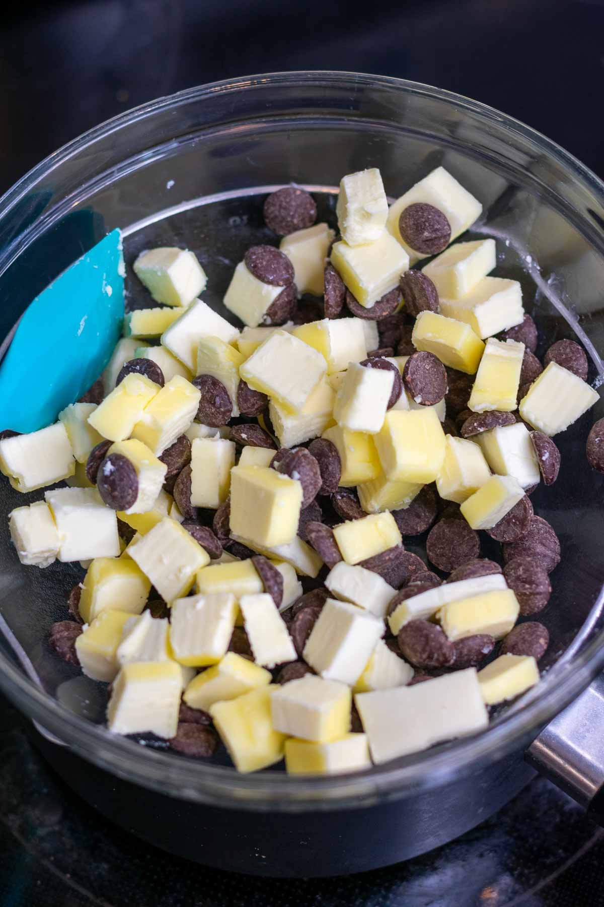 Cubed butter and chocolate chips in a bowl with a spatula over a stovetop.