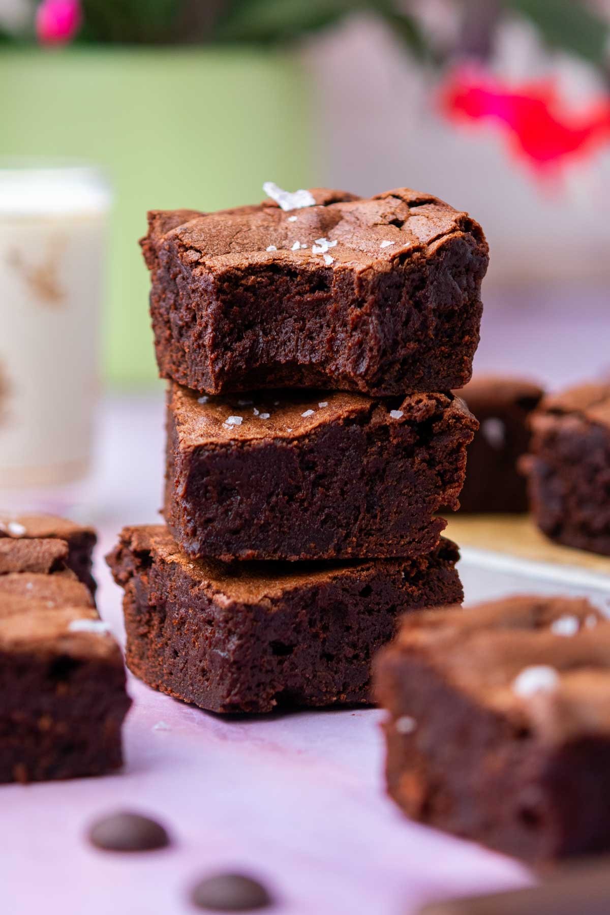 Stack of three fudgy sourdough brownies with a glass of milk and a flower in the background