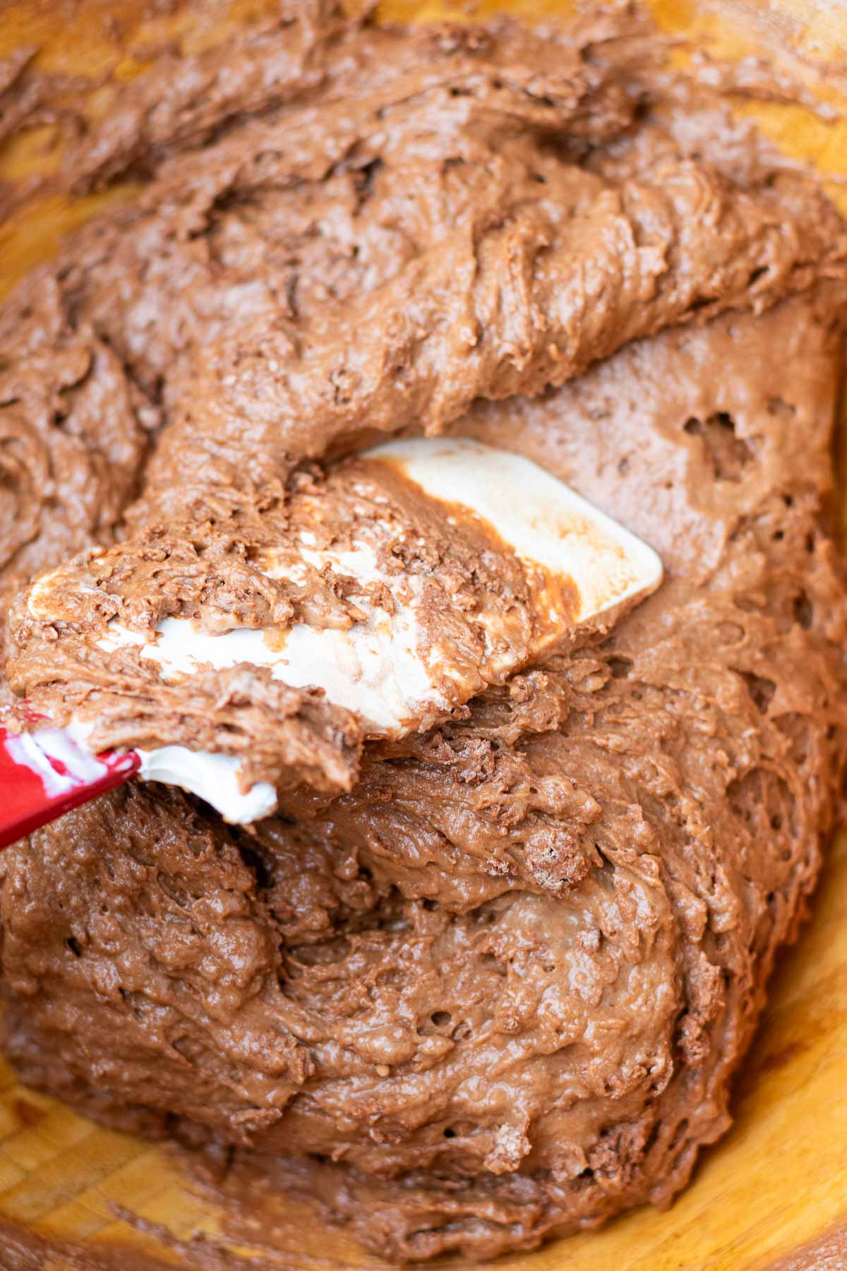 Mixing sourdough chocolate muffin batter in a bowl with a spatula.
