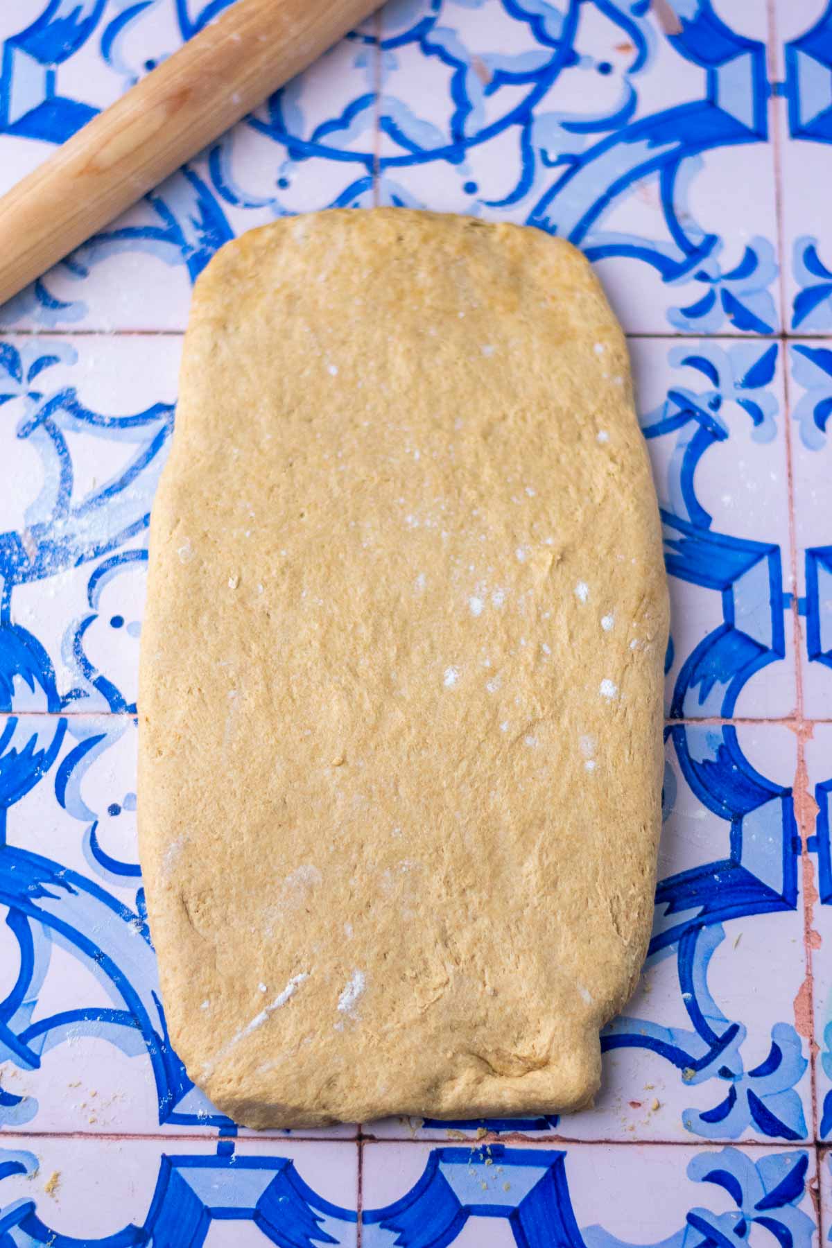 Rolling out einkorn sourdough sandwich bread dough on counter with a rolling pin into rectangular slab.