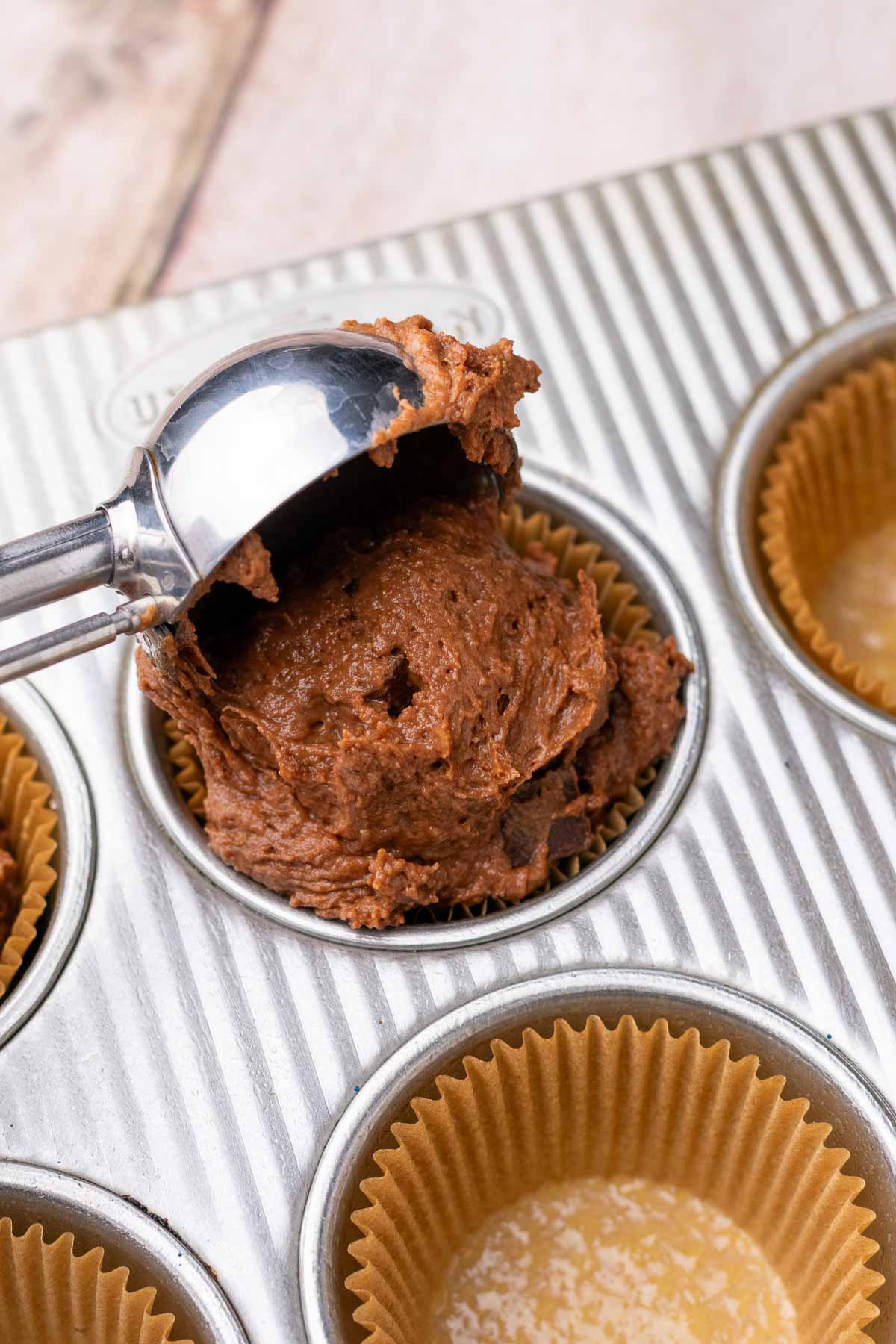 Scooping sourdough chocolate muffin batter into a lined muffin pan.