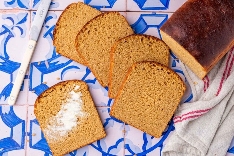 Slices of einkorn sourdough sandwich bread spread out and one has butter on it.