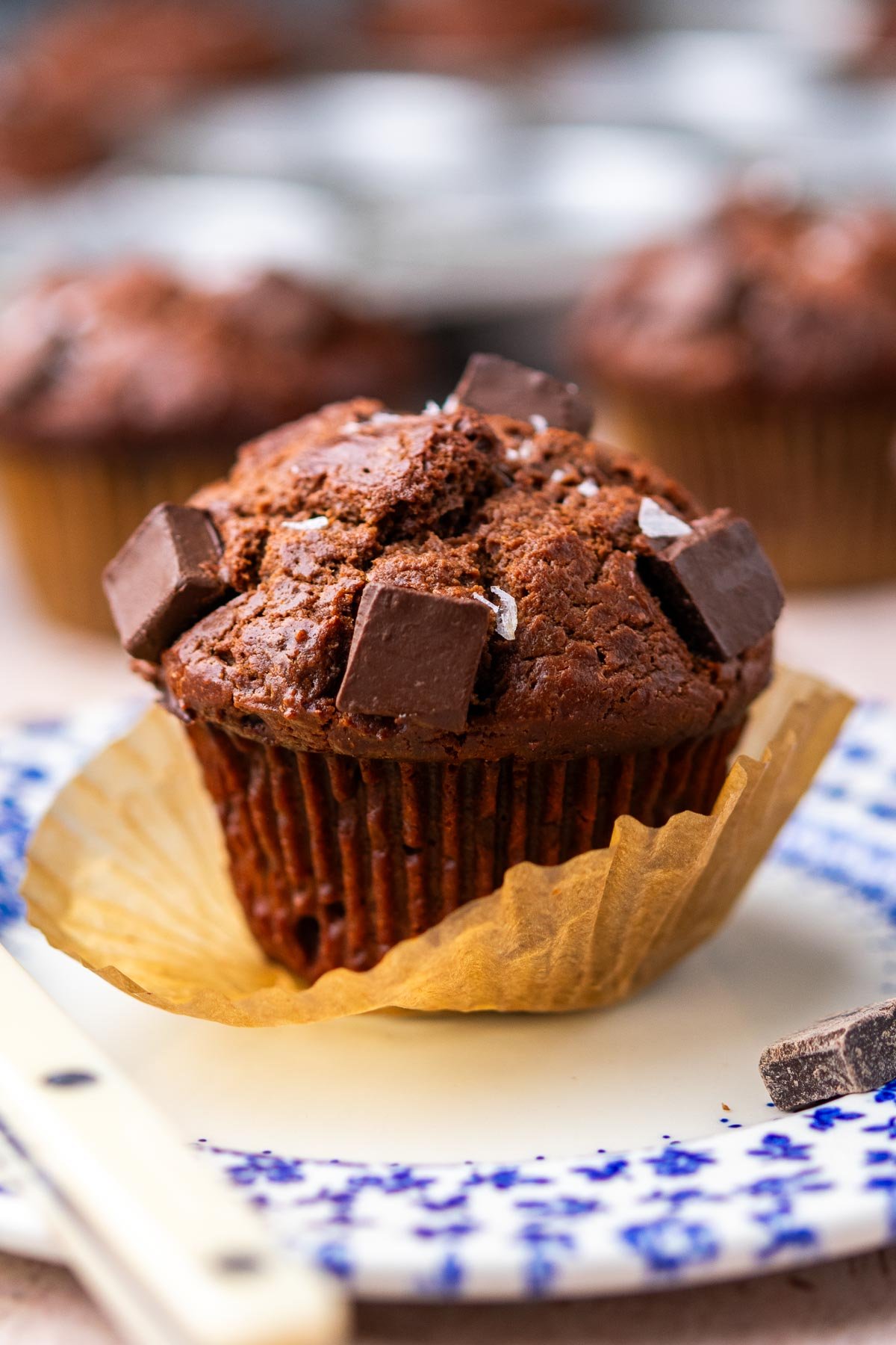Sourdough chocolate muffins with chocolate chunks and flaky salt on a plate with the muffin paper peeling off.