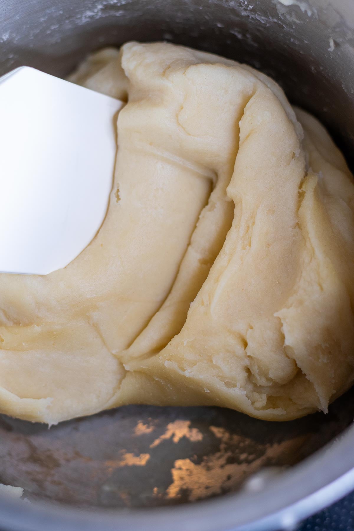 Cooking sourdough pate a choux in a saucepan with a spatula.