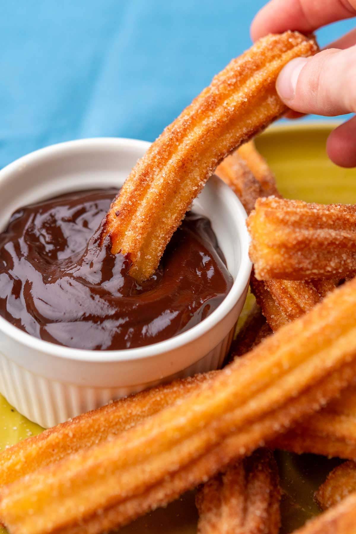 Hand dipping sourdough churro in chocolate sauce.