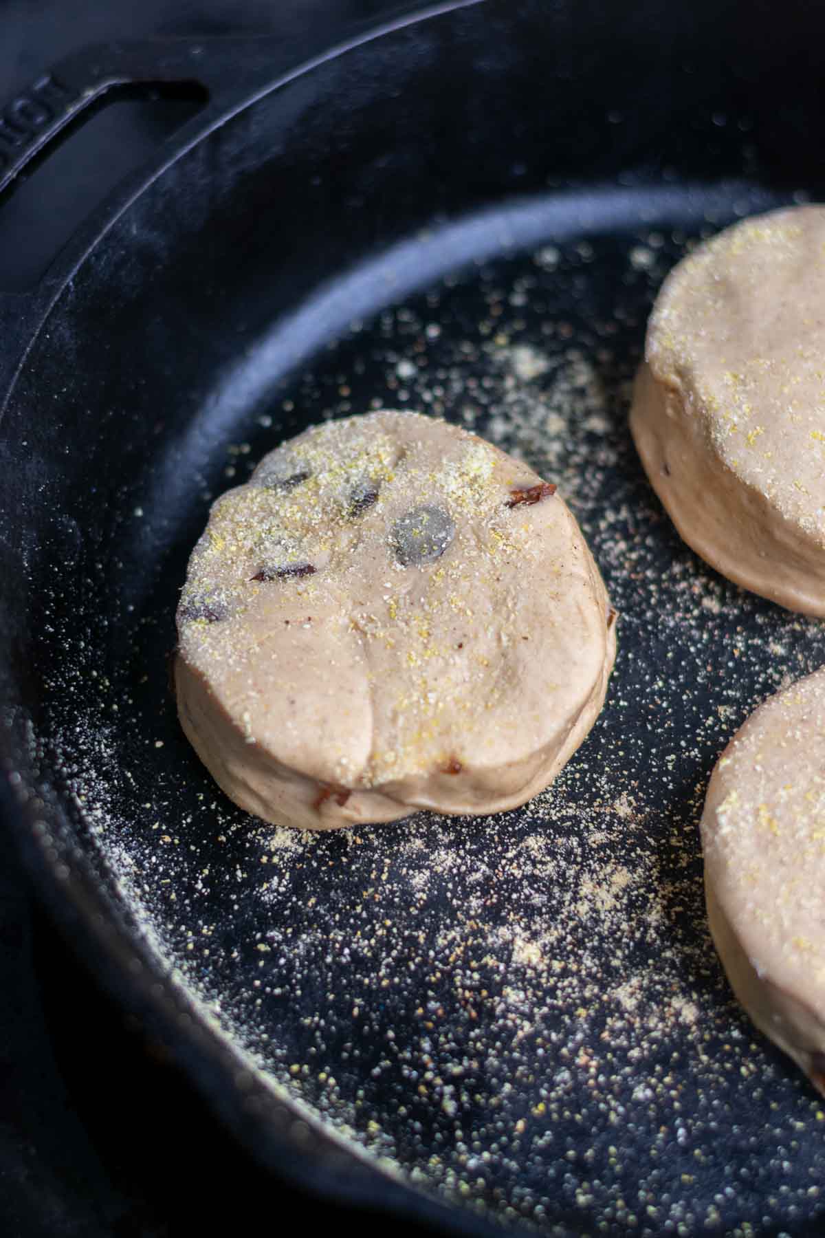 Griddling sourdough cinnamon raisin english muffins in a cast-iron skillet.