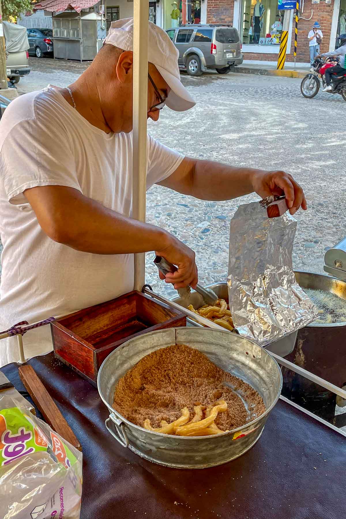 Man in mexico on street tossing fried churros in cinnamon sugar.