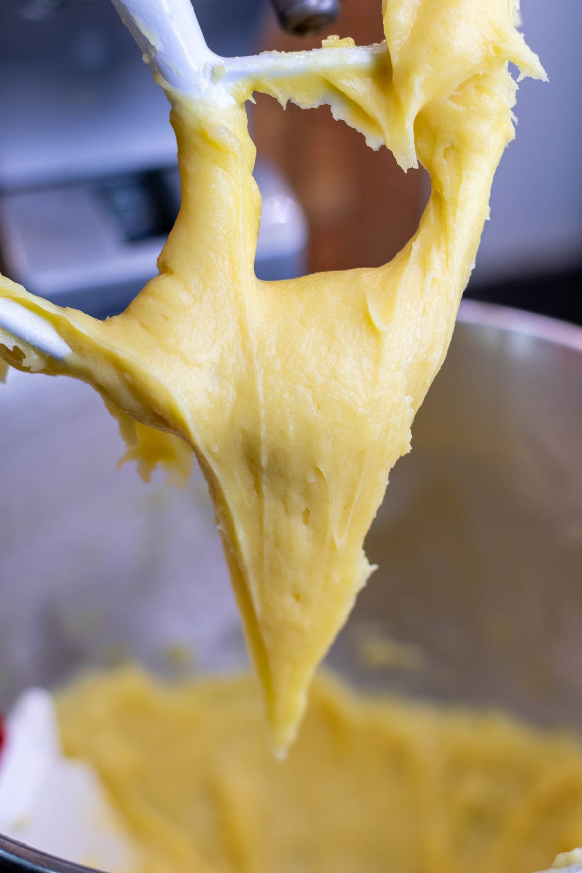 Mixed sourdough pate a choux in stand mixer lifted from bowl on paddle attachment.