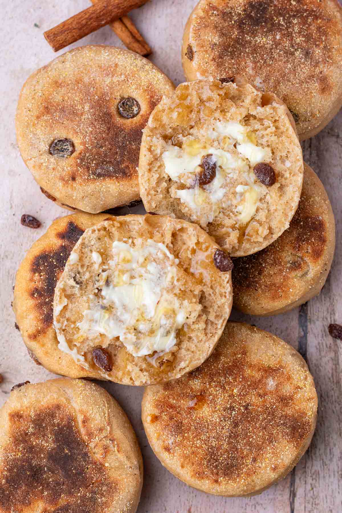 Many sourdough cinnamon raisin english muffins with one sliced on top with butter and honey.