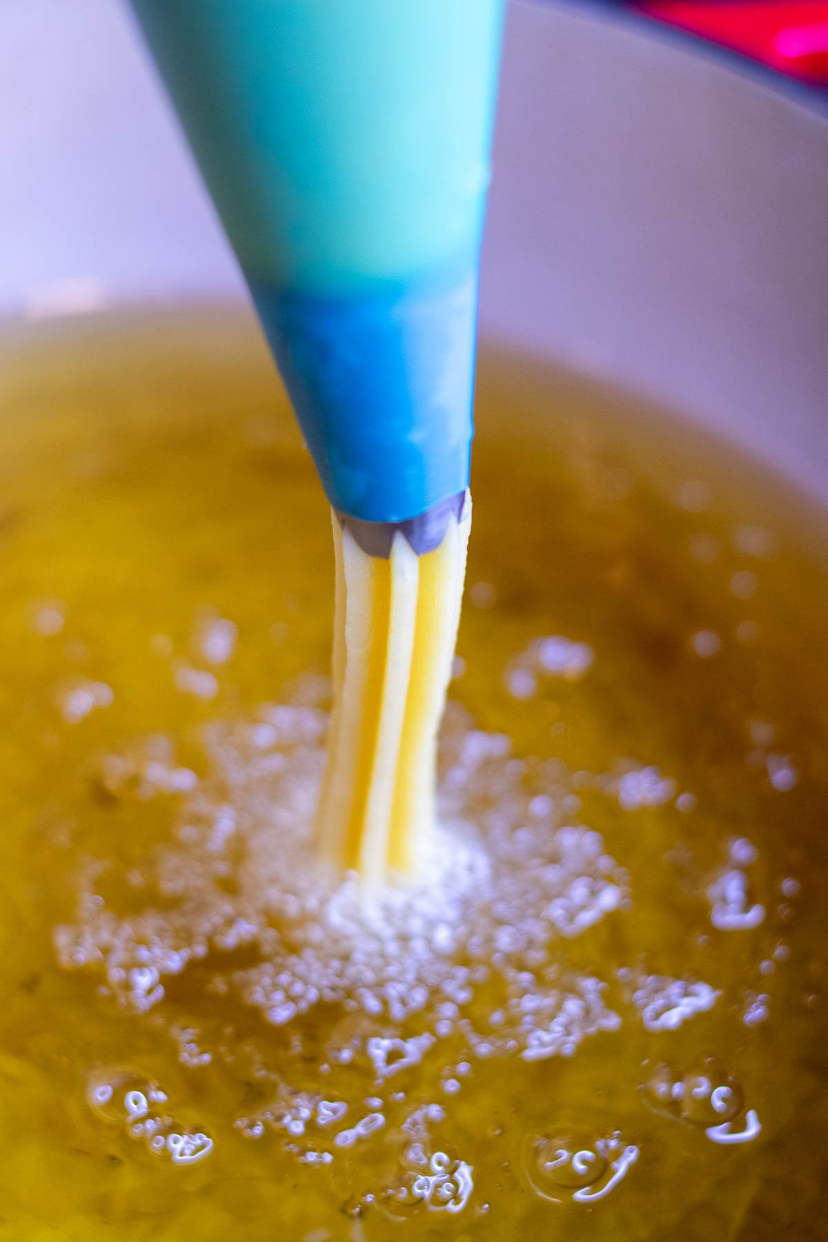Piping sourdough churros into hot frying oil with piping bag.