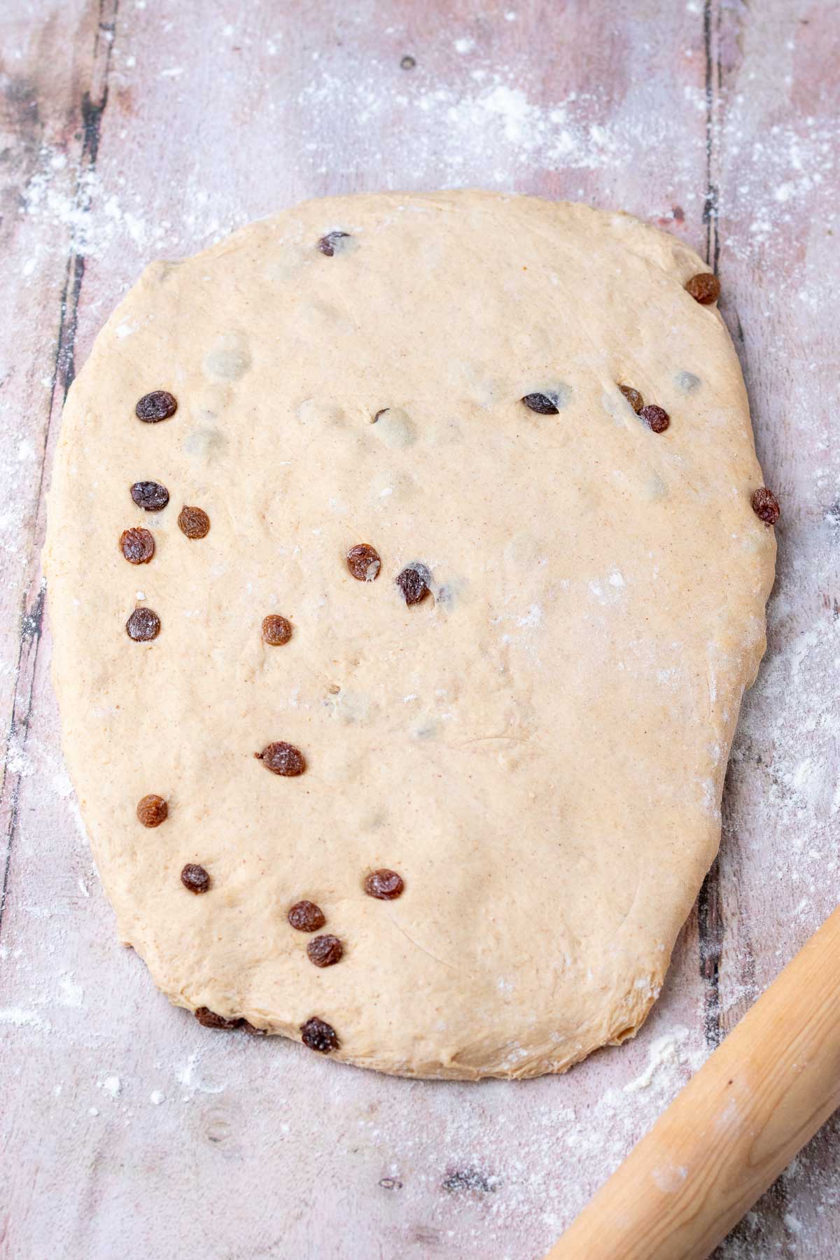 Rolled out sourdough cinnamon raisin english muffin dough with a rolling pin.