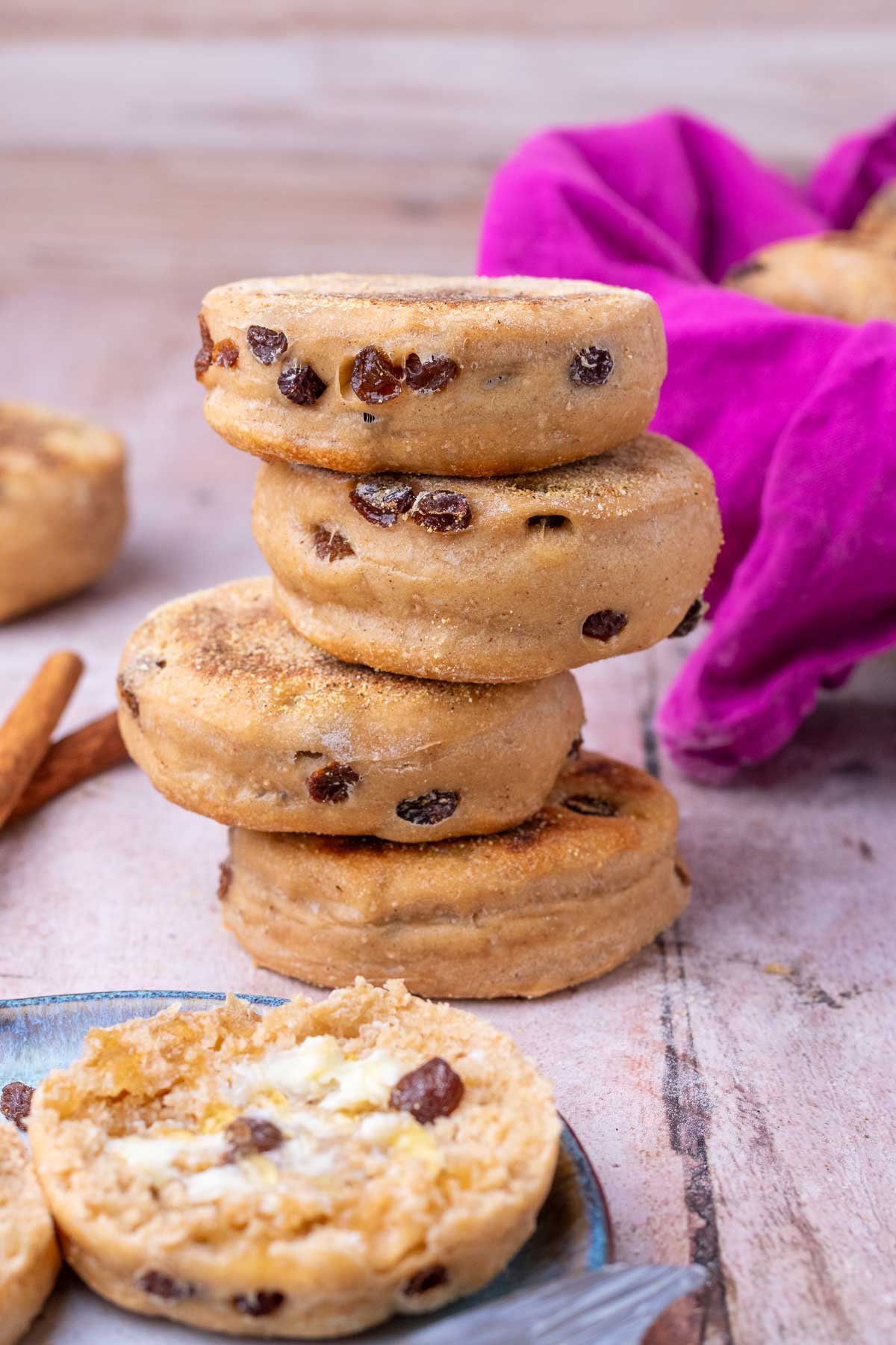 Stack of four sourdough cinanmon raisin english muffins with one cut open with butter on a plate in front.