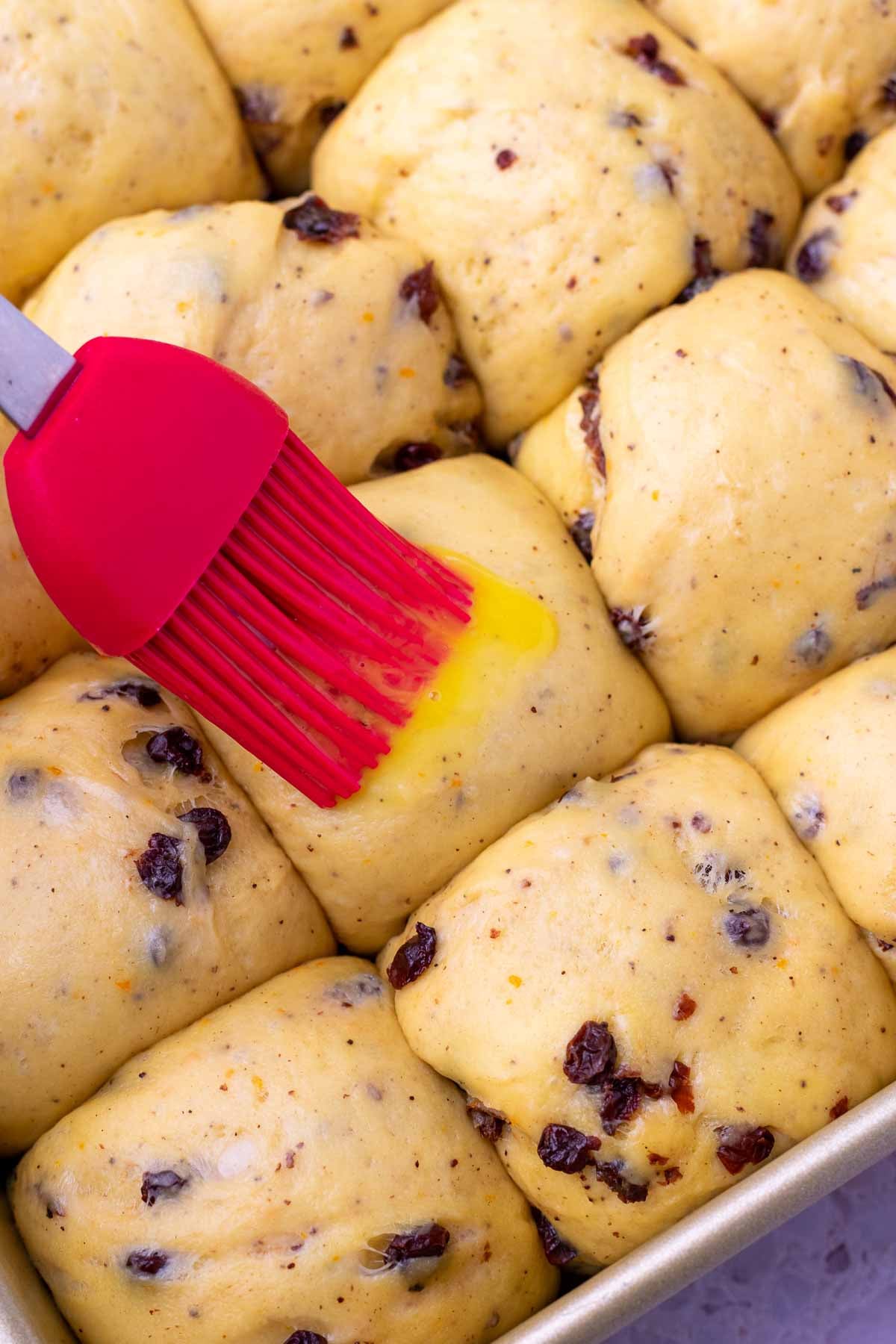 Brushing egg wash on sourdough hot cross buns before baking.