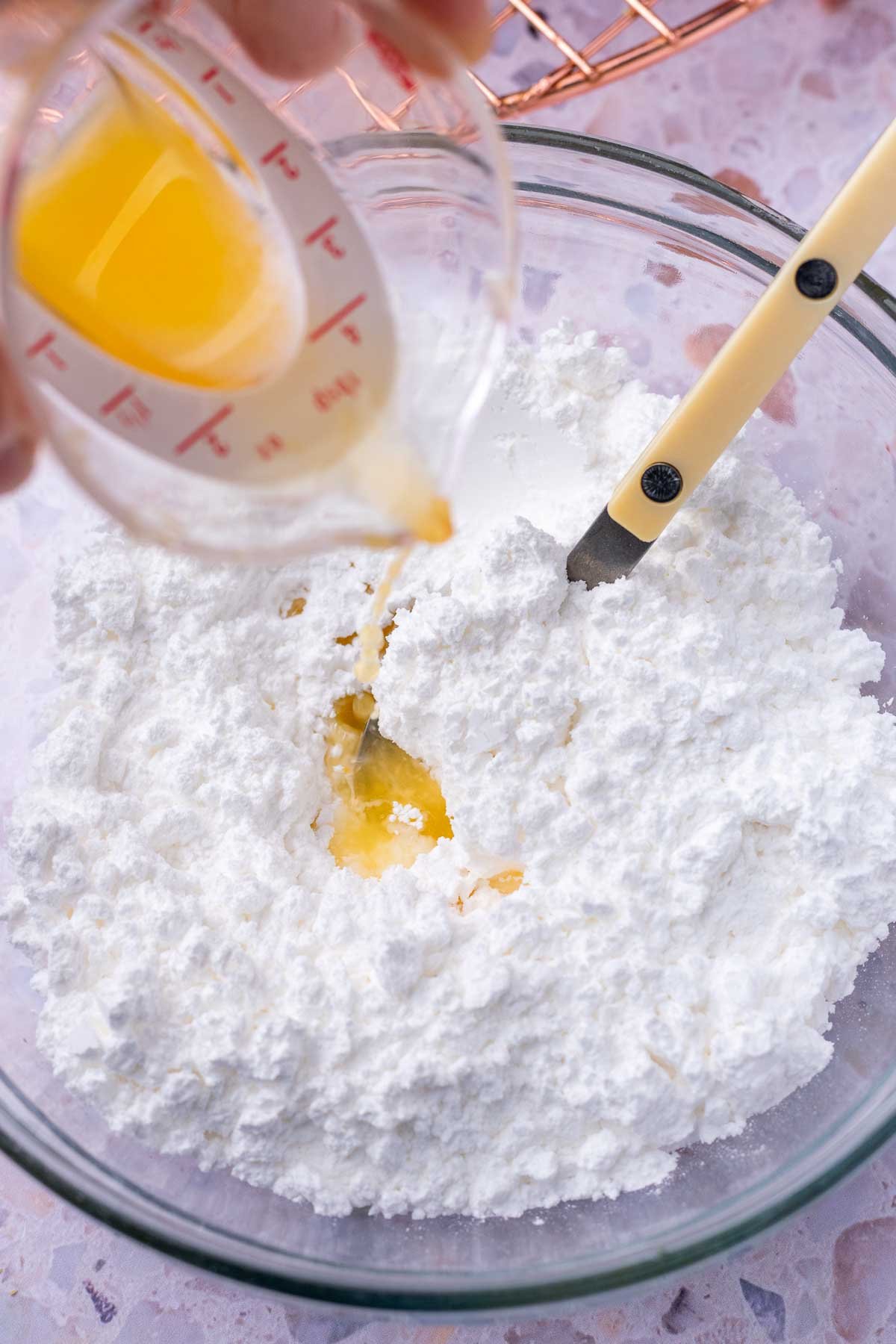 Pouring orange juice into bowl with powdered sugar and a spoon.
