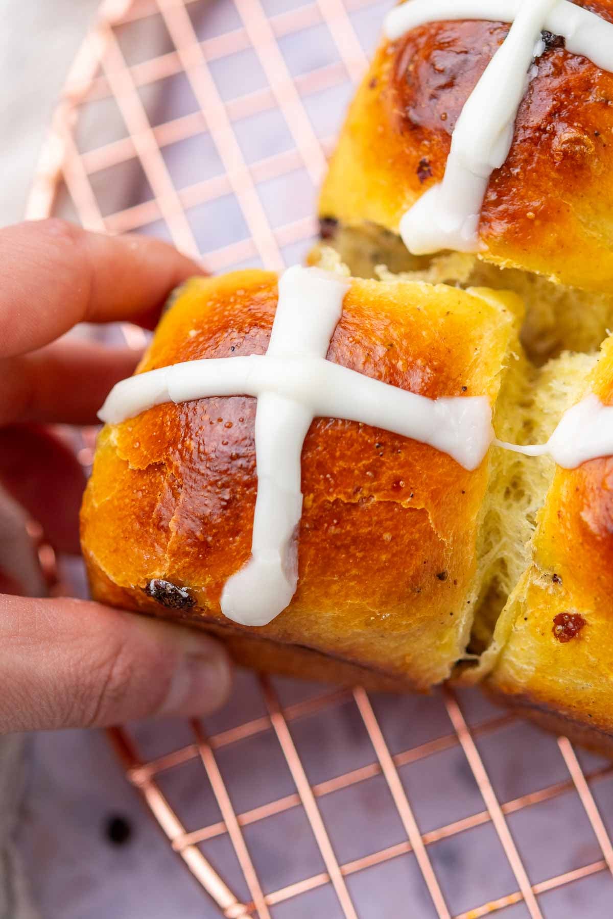 Hand pulling apart a sourdough hot cross bun on a wire rack.