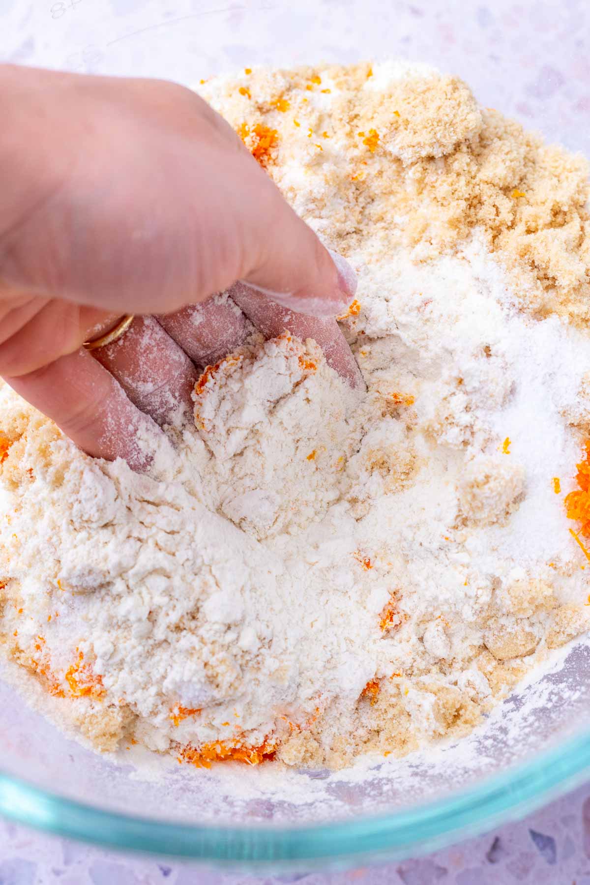 Hand rubbing orange zest in a bowl of dry ingredients.