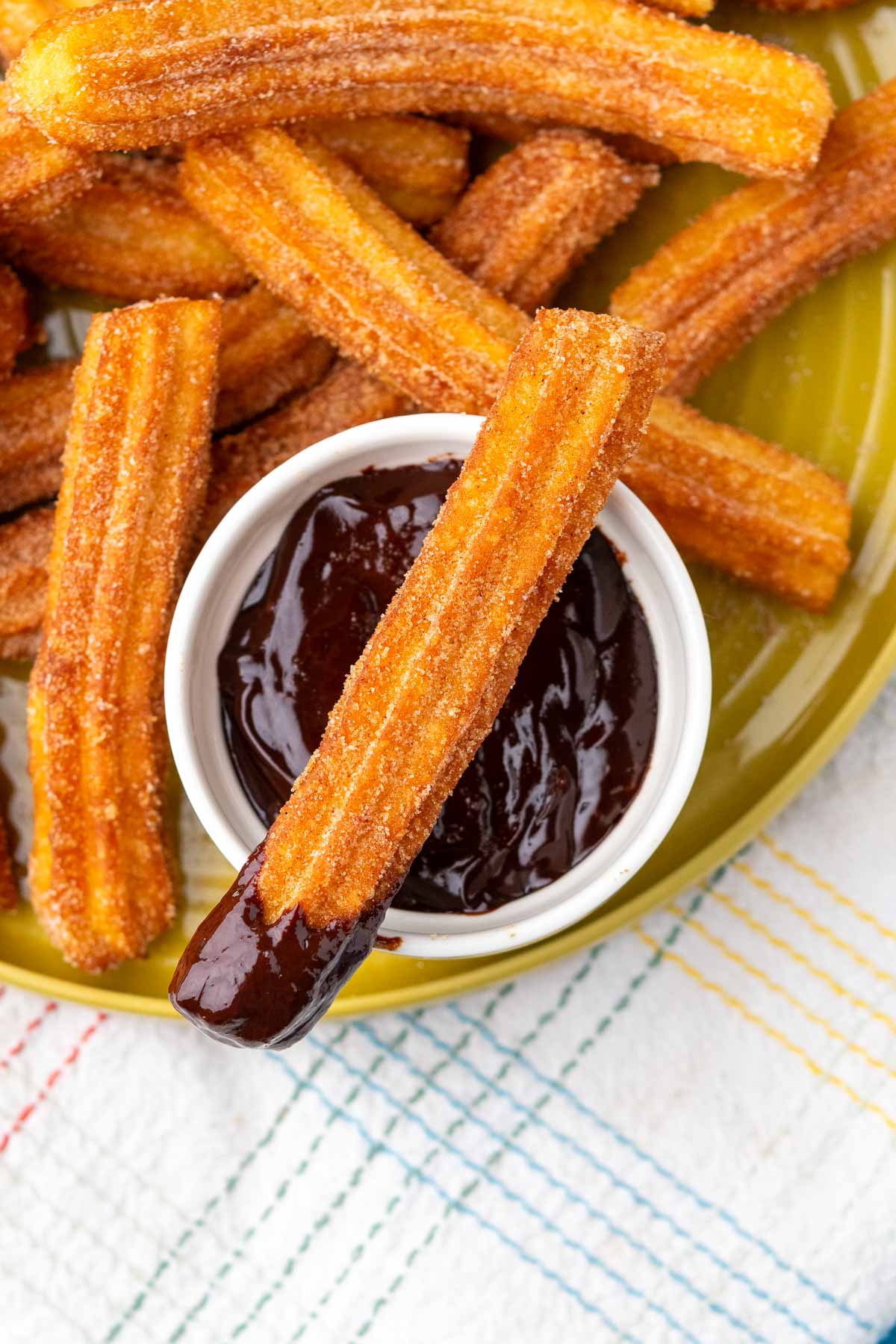 Sourdough churros on a plate with one dipped in chocolate dipping sauce over a bowl of chocolate sauce.