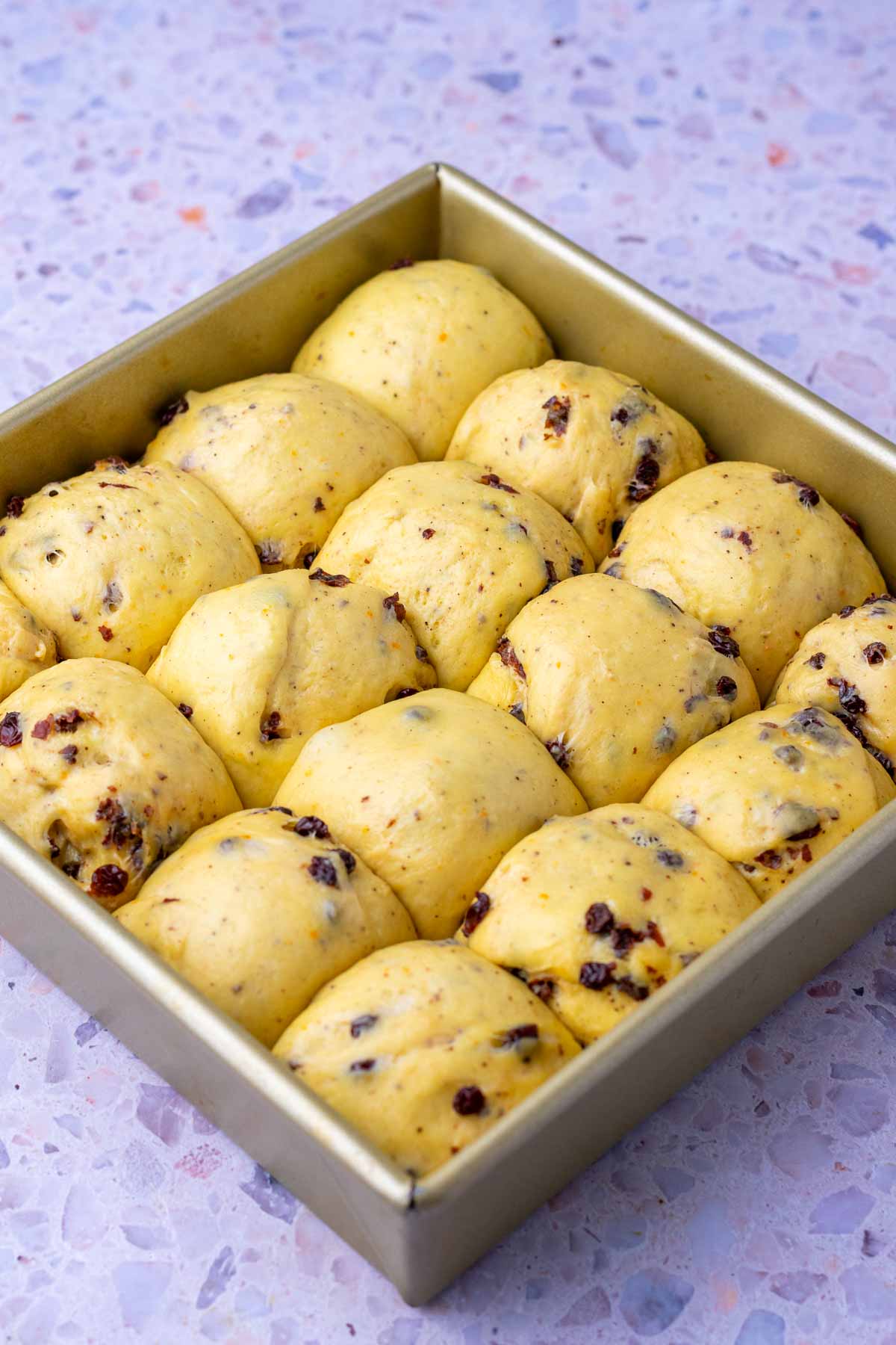 Proofed sourdough hot cross buns in a 9-inch square baking pan.