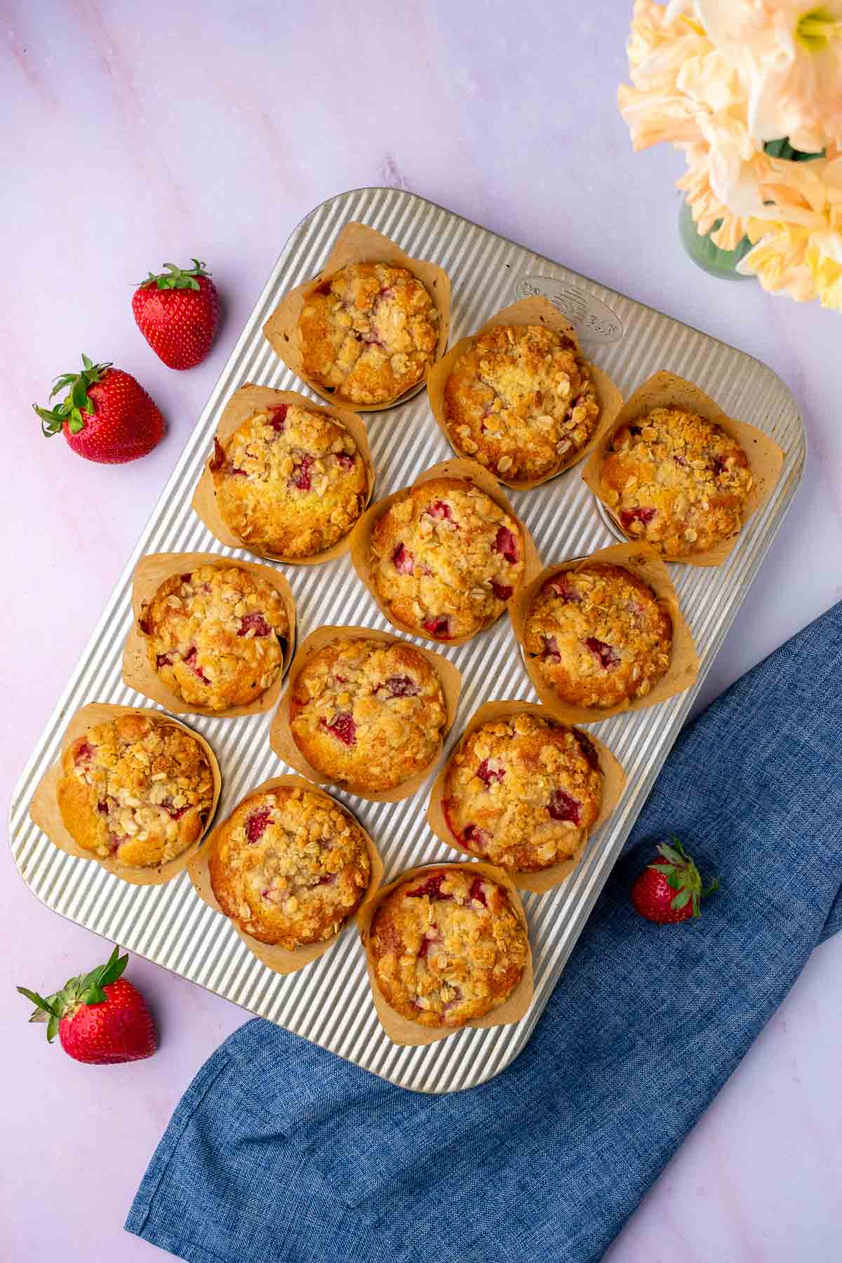 Baked Sourdough strawberry muffins in a baking pan with strawberries and a tea towel surrounding the pan.