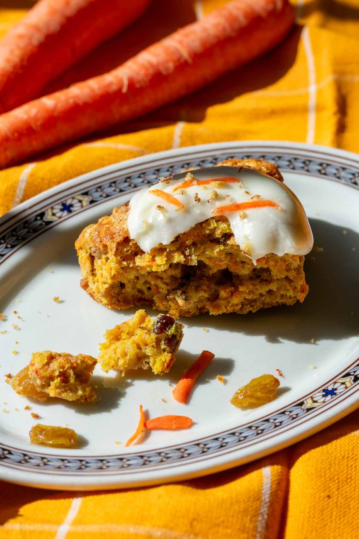 Bite taken out of a sourdough carrot cake scone on a plate with carrots in the background.