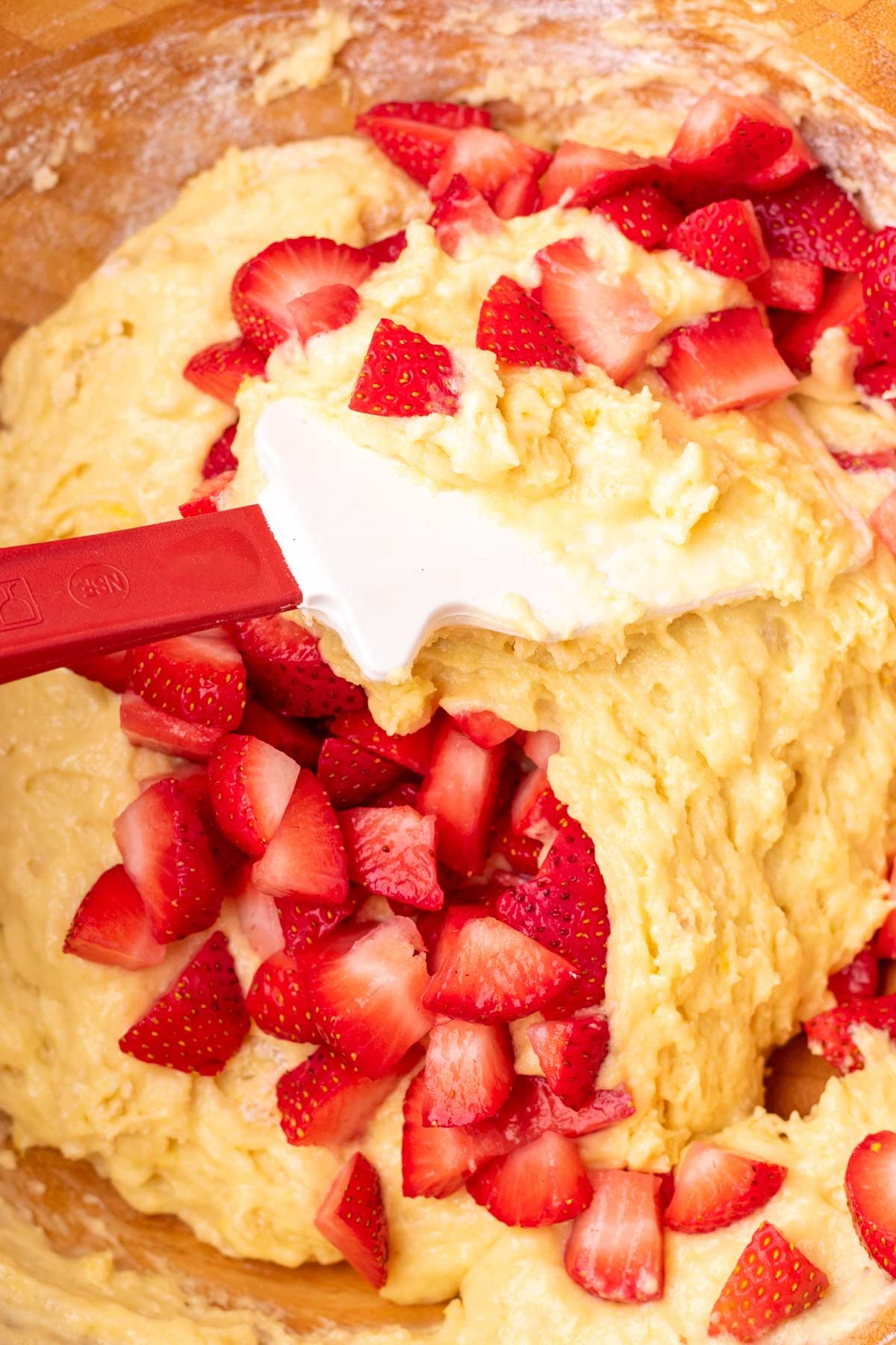Spatula folding fresh strawberries into Sourdough strawberry muffin batter in a bowl.