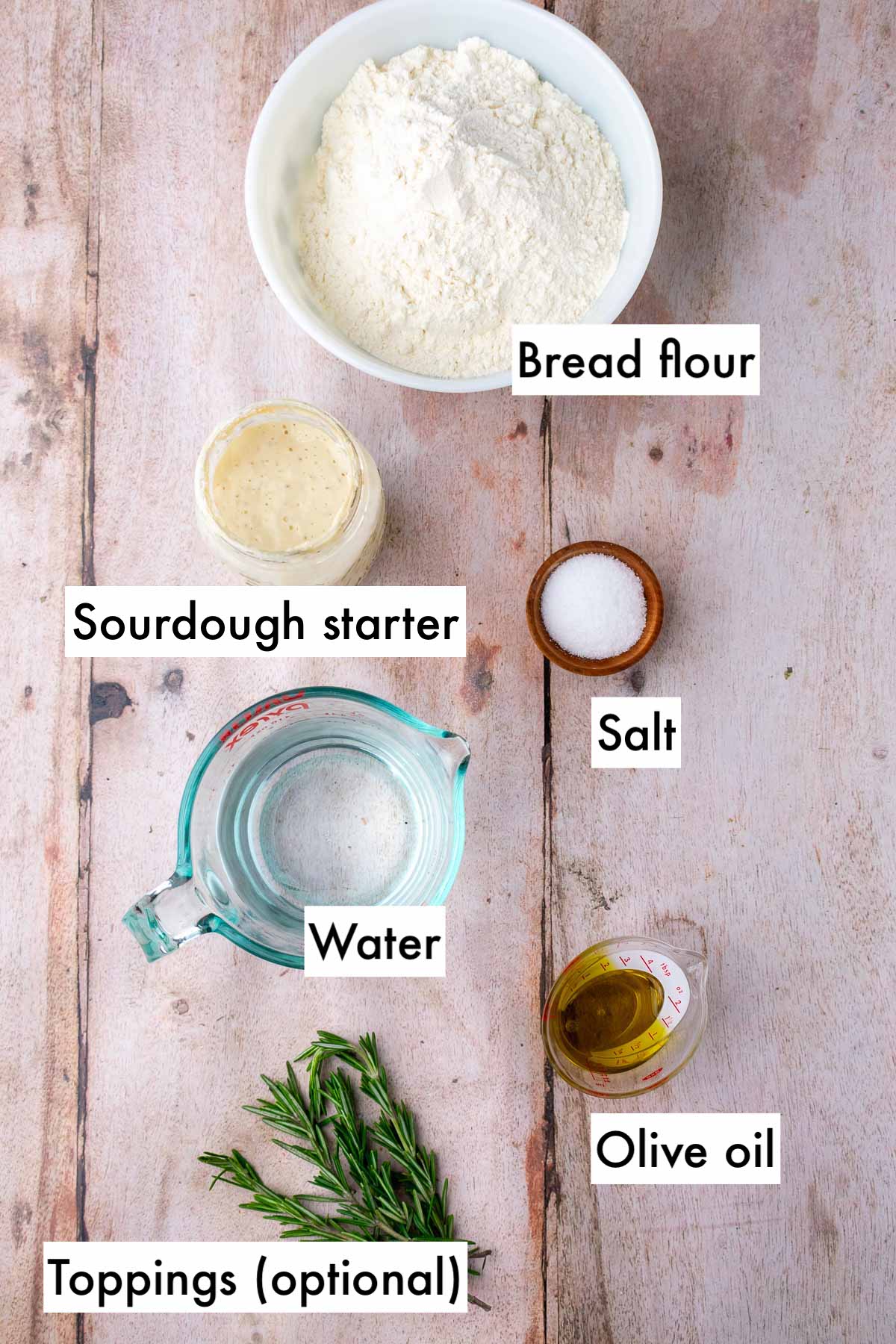 Labeled bowls of ingredients needed for sourdough focaccia including bread flour, salt, sourdough starter, olive oil, water, and optional toppings.