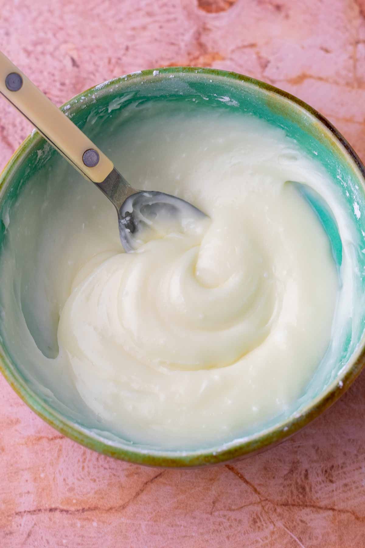 Small mixing bowl with mixed cream cheese glaze and a spoon.