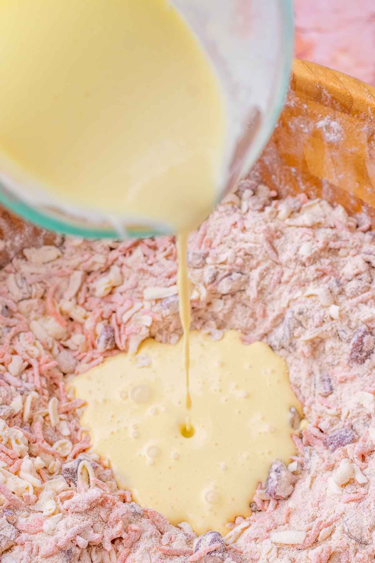 Pouring wet ingredients into bowl of dry ingredients for sourdough carrot cake scones.