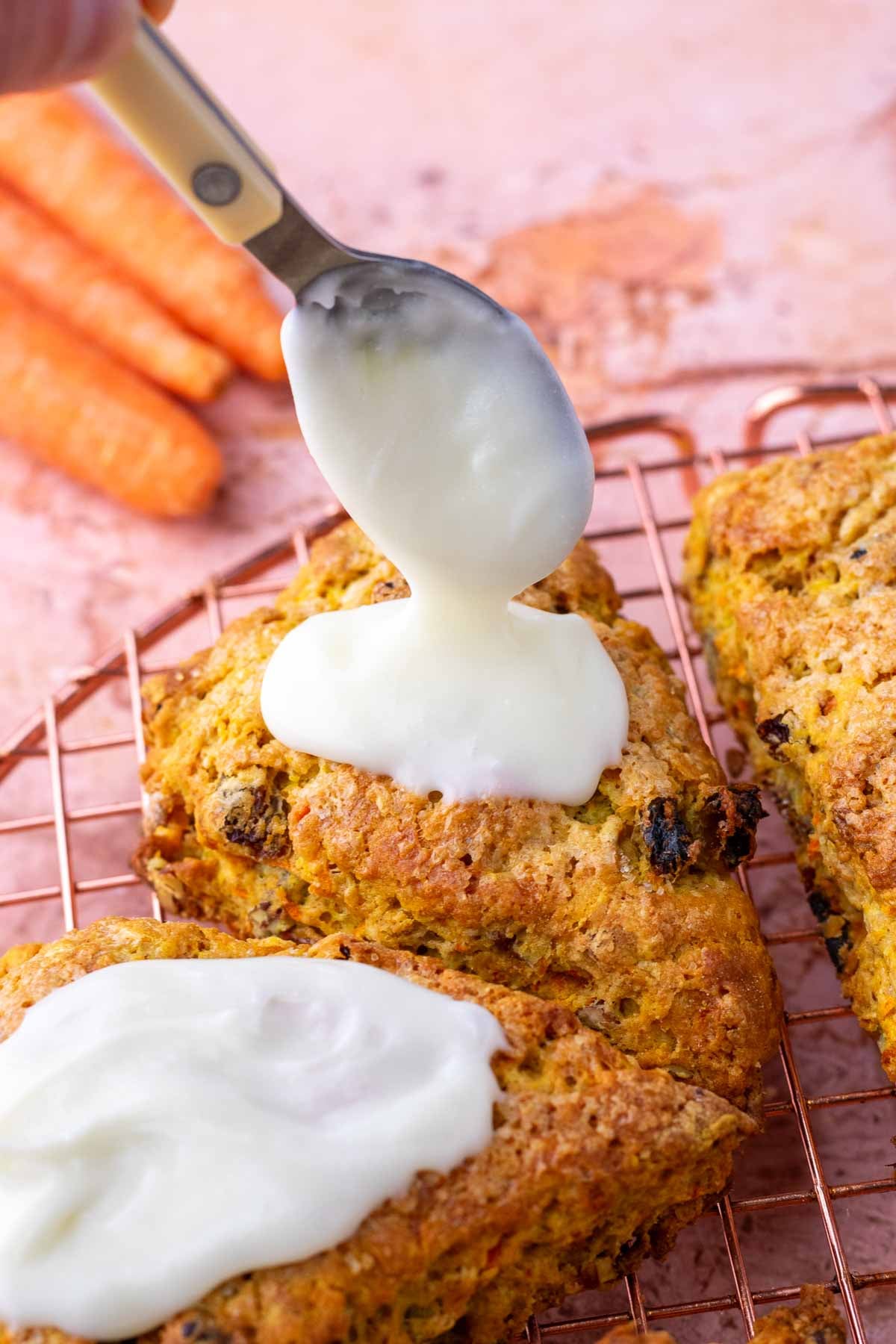Spooning cream cheese glaze onto sourdough carrot cake scones.