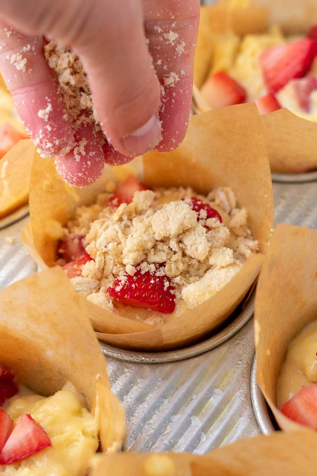Hand sprinkling oat crumb topping onto Sourdough strawberry muffins.