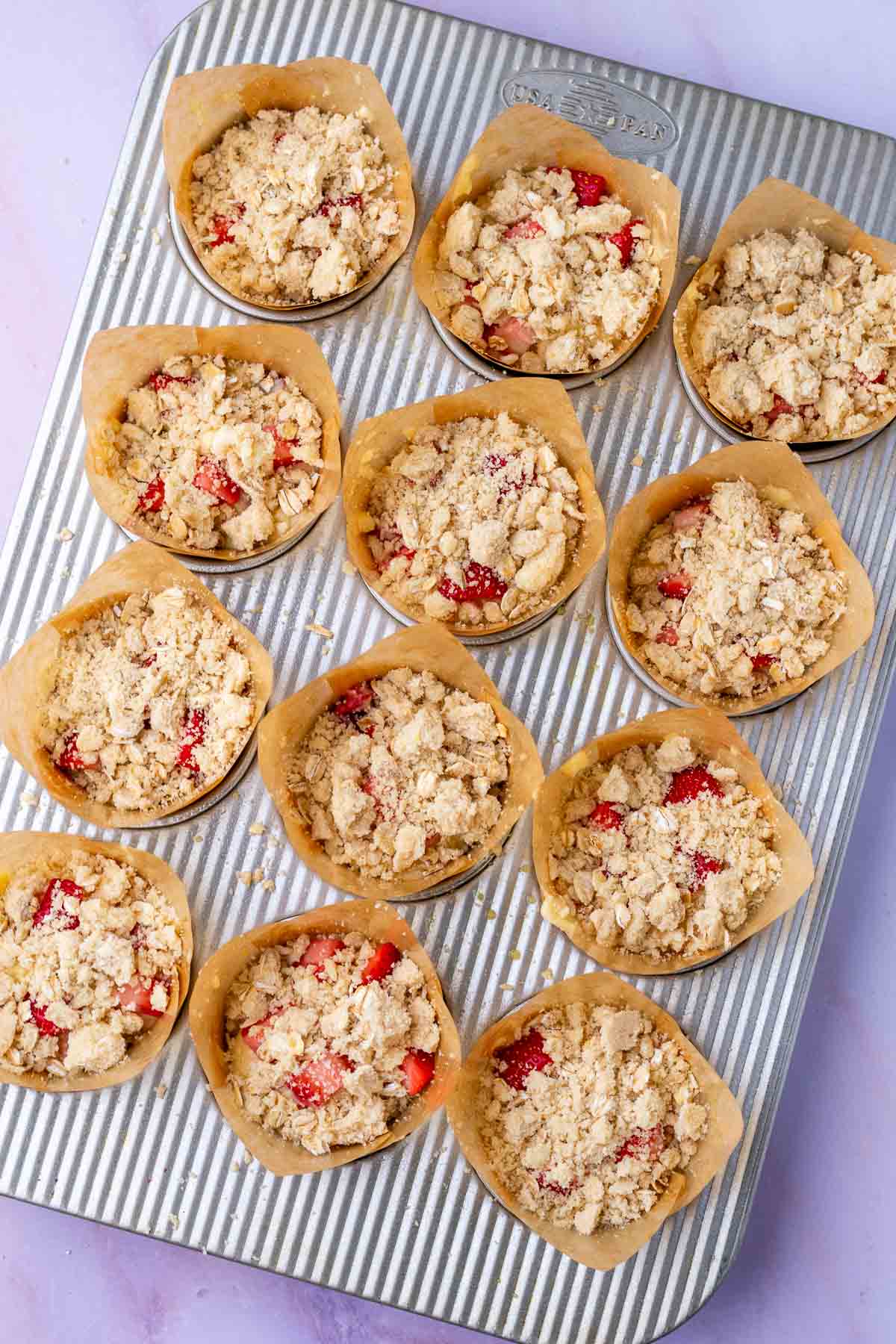 Unbaked Sourdough strawberry muffins with oat crumb topping in paper liners in a baking pan.