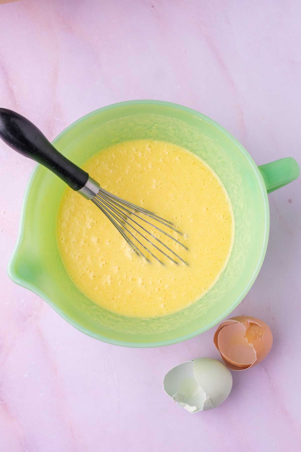 Bowl of wet ingredients mixed for Sourdough strawberry muffin with a whisk and egg shells.