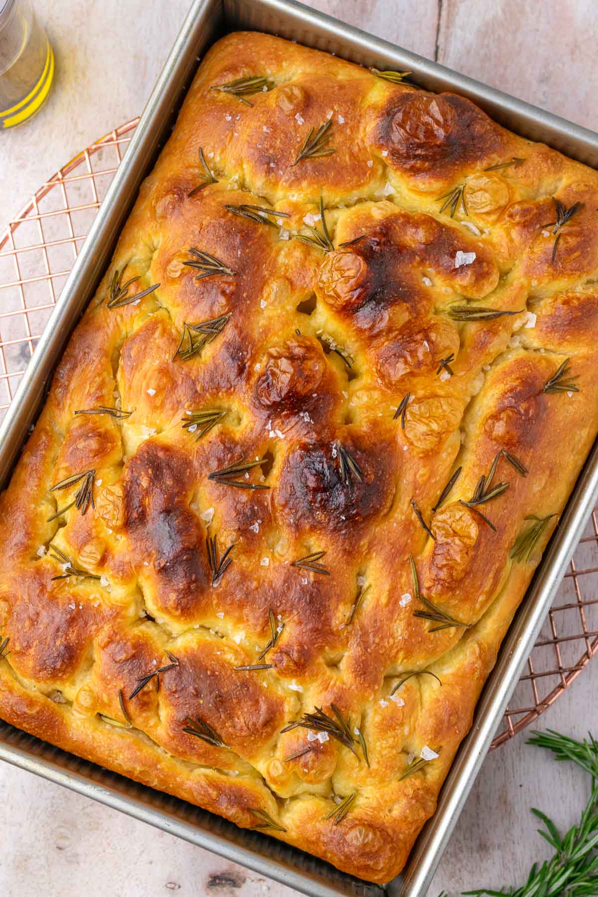 Baked sourdough focaccia in baking pan cooling on wire rack.