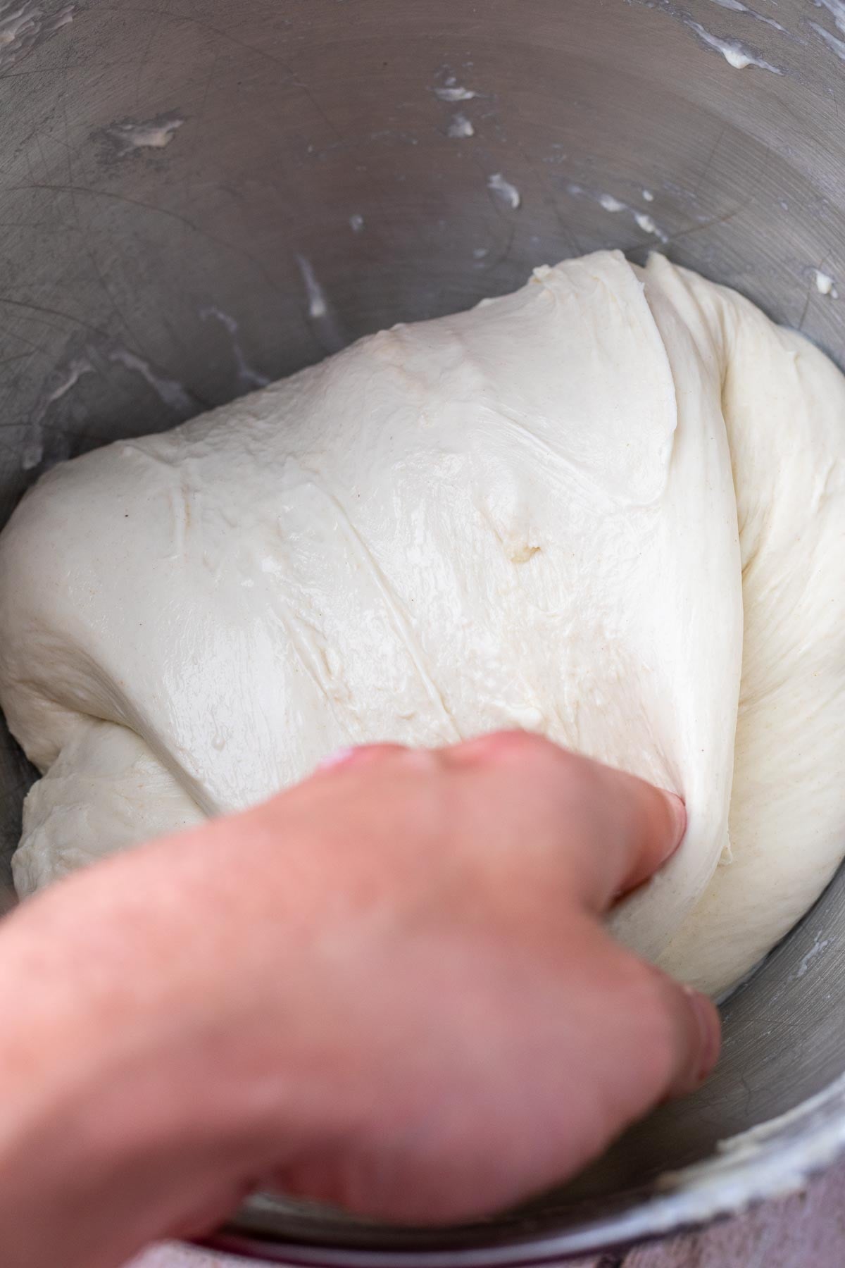 Hand folding sourdough focaccia dough in bowl.