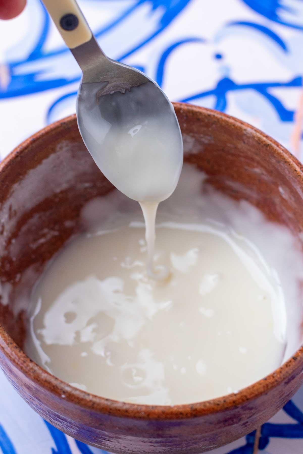 Spoon dripping mixed lemon glaze from a bowl.