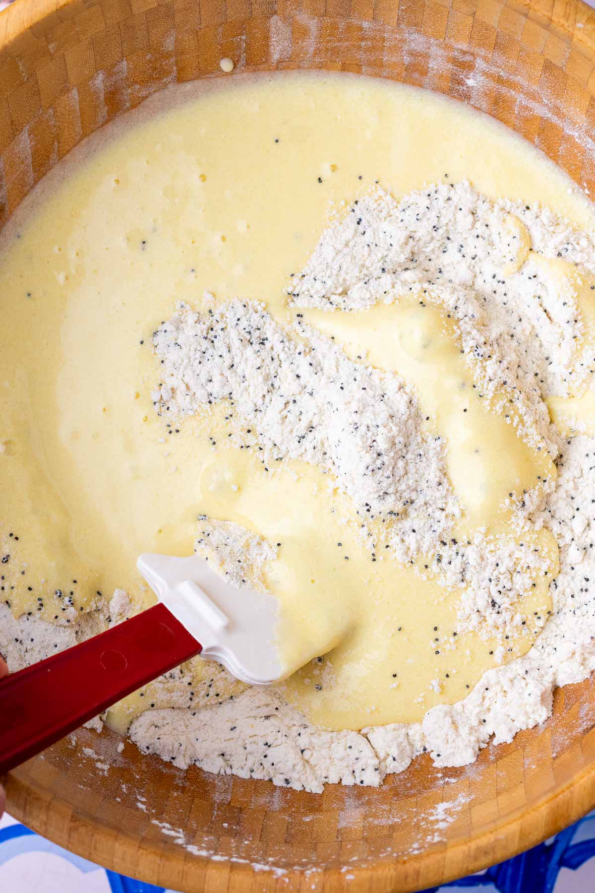 Folding wet ingredients into dry for sourdough lemon poppy seed muffins in a large bowl with a spatula.