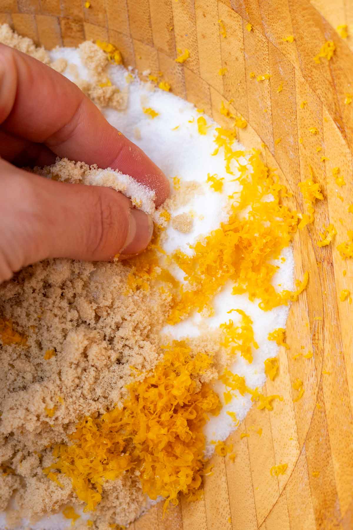 Hand rubbing lemon zest into sugar in a bowl.