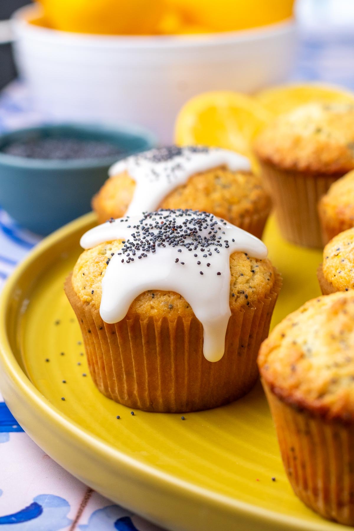 Sourdough lemon poppy seed muffins on a plate with lemon glaze dripping and a bowl of lemons in the background.