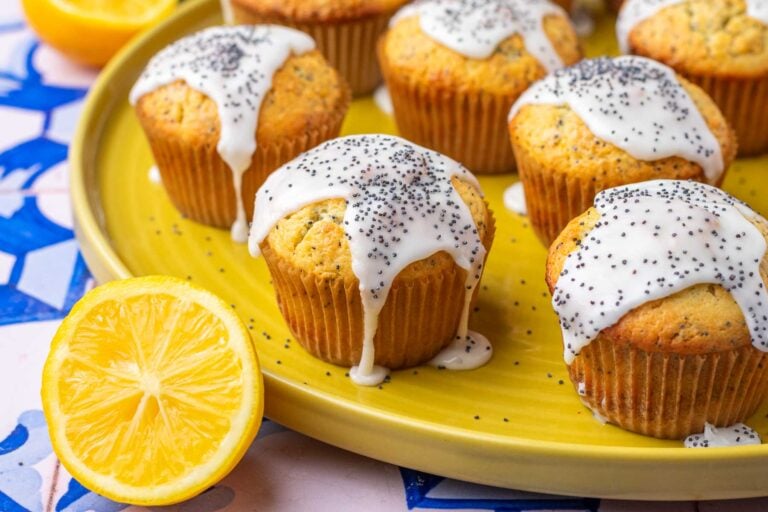 Sourdough lemon poppy seed muffins on a plate with dripping lemon glaze and a sliced lemon.