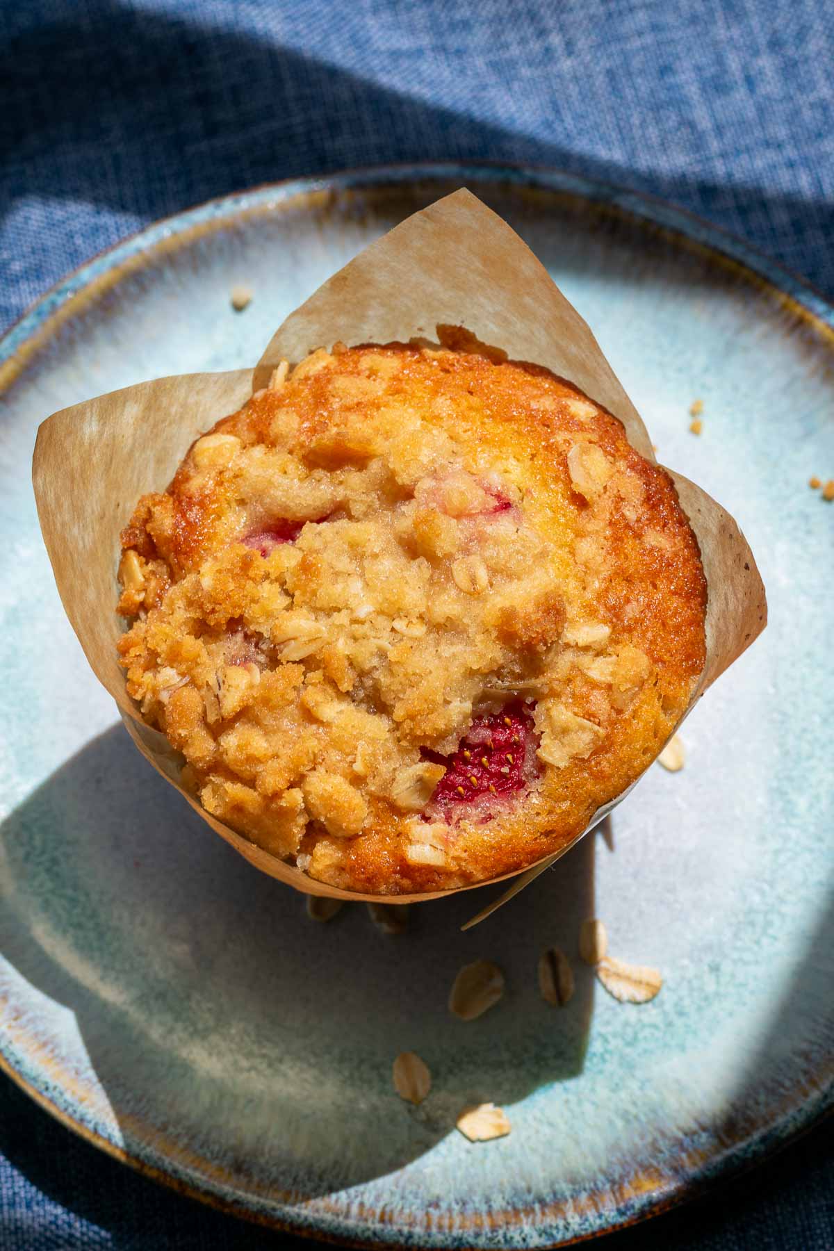 Sourdough strawberry muffin with crumb topping in a paper liner on a plate. 
