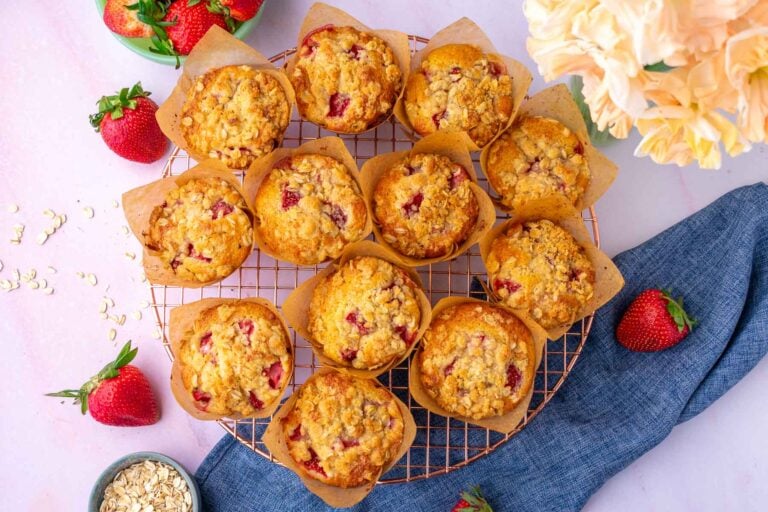 Sourdough strawberry muffins with crumb topping on a wire rack with strawberries, oats, and flowers.