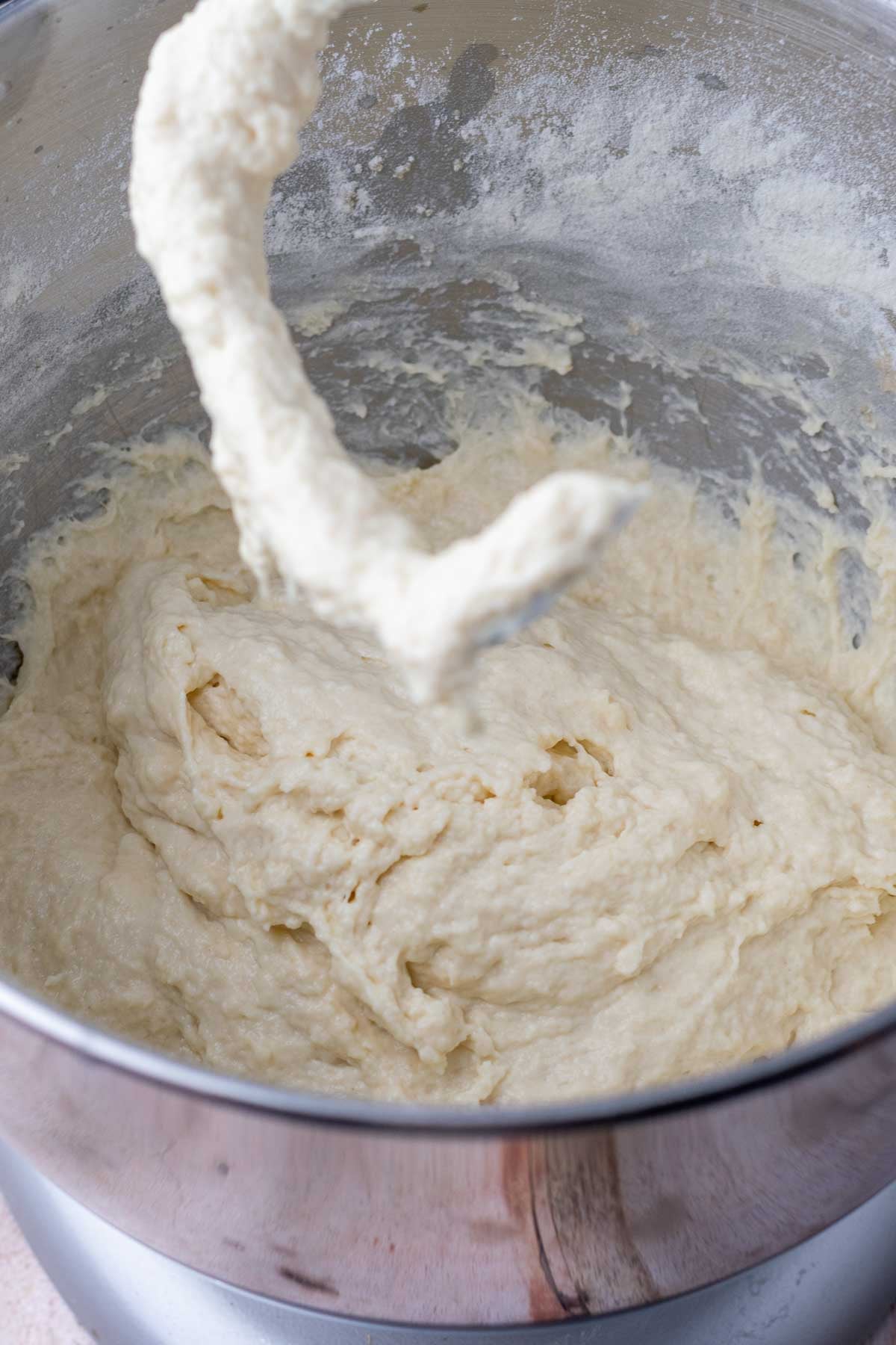 Bowl of a stand mixer with dough hook attachment with wet sourdough focaccia dough at the start of mixing.