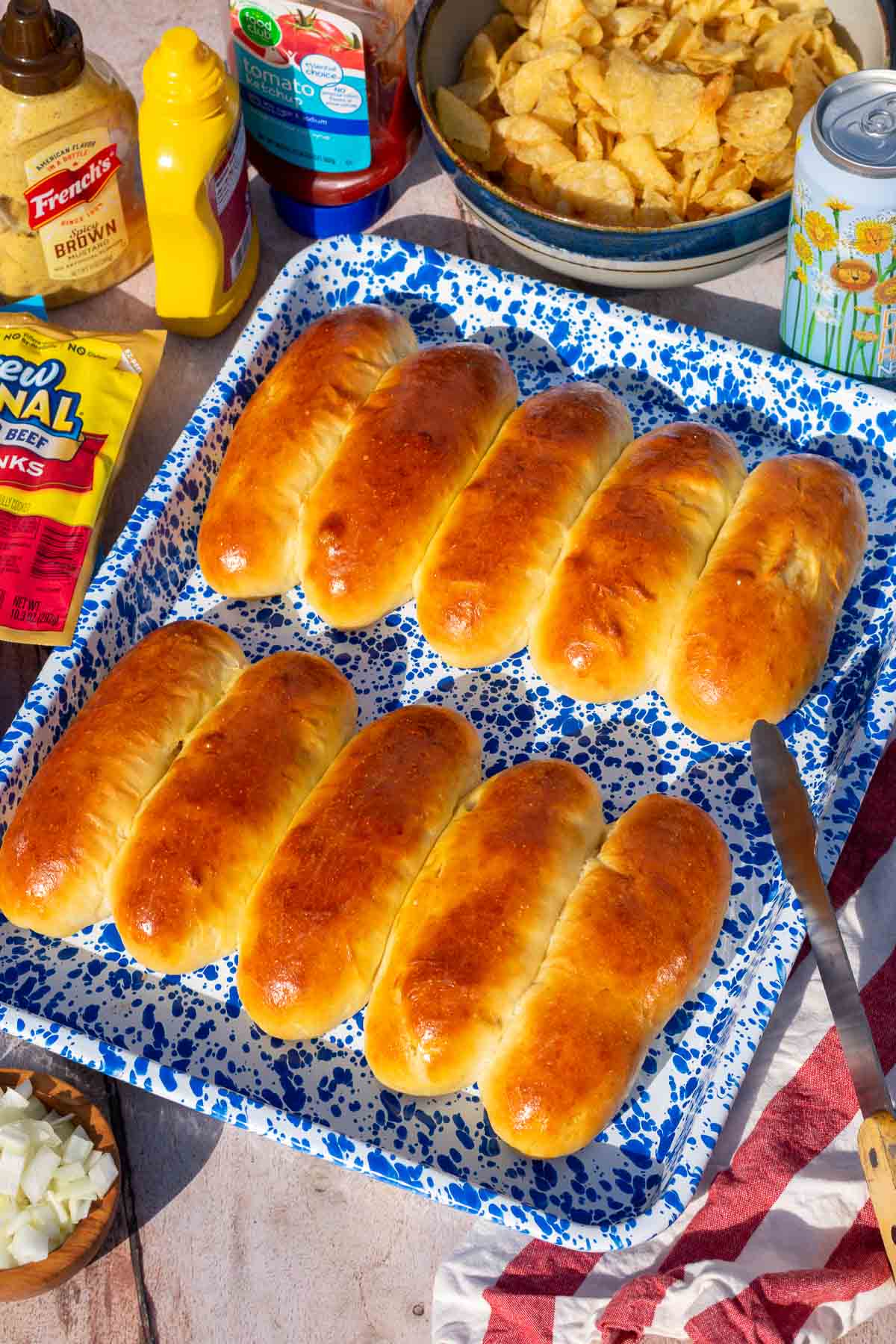 Baked sourdough hot dog buns on a blue splatter enamelware platter with condiments and chips around the platter.